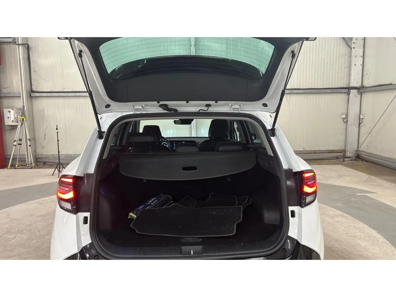 Coffre ouvert d'un KIA Sportage blanc 2022 vu de l'arrière avec tapis de sol et hayon relevé en intérieur d'entrepôt.