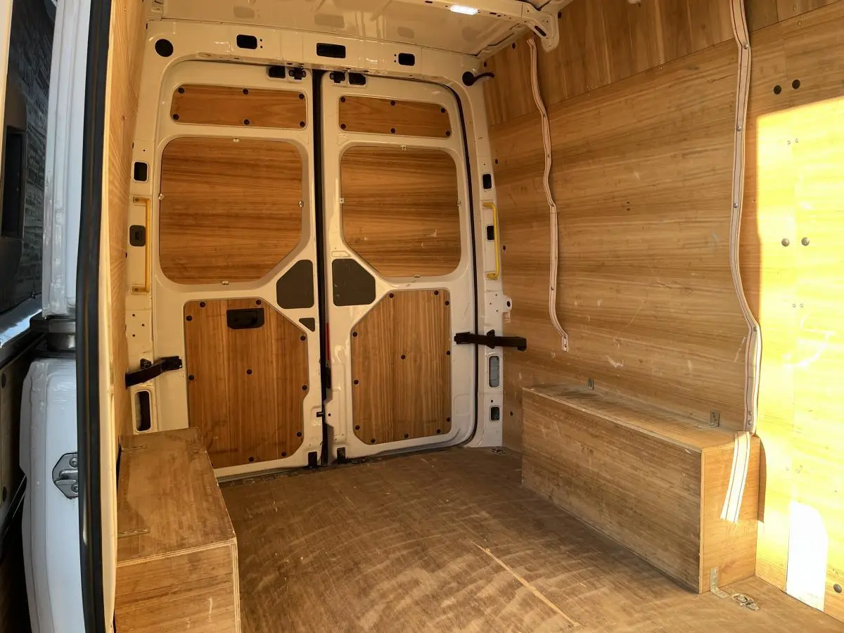 Intérieur du fourgon Volkswagen Crafter blanc vu de l'arrière, avec aménagements en bois sur les parois et le plancher.