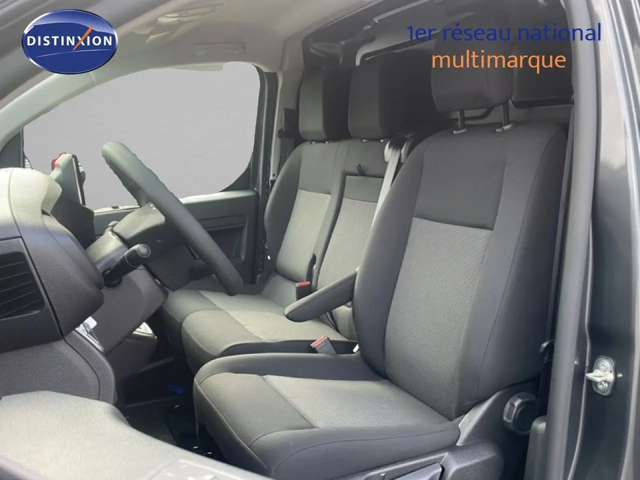 Vue intérieure côté conducteur du Citroën Jumpy gris titane, montrant les sièges avant en tissu noir et la console.