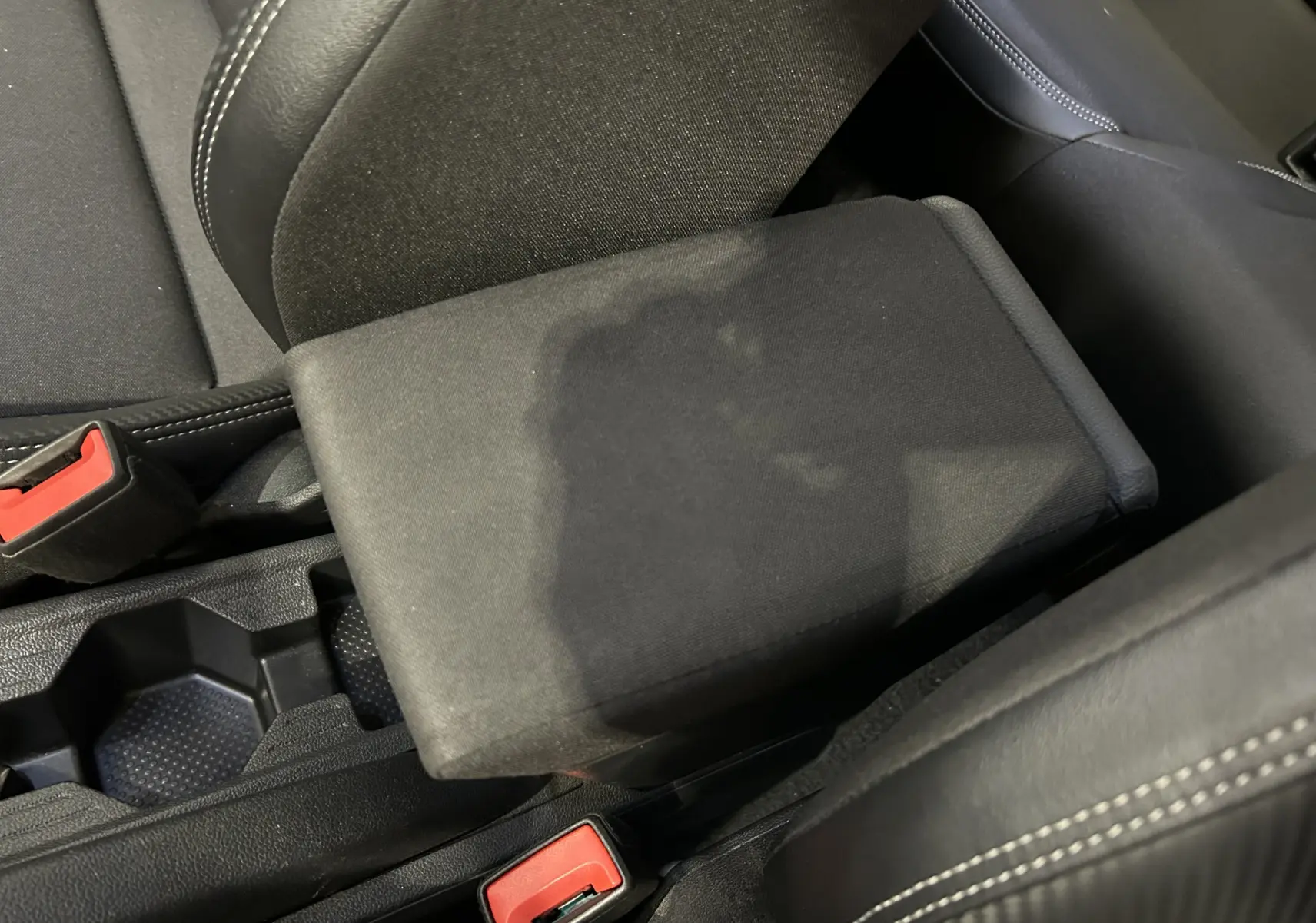 Gros plan sur l'accoudoir central noir et les sièges en tissu noir avec surpiqûres blanches dans un Volkswagen Taigo blanc.