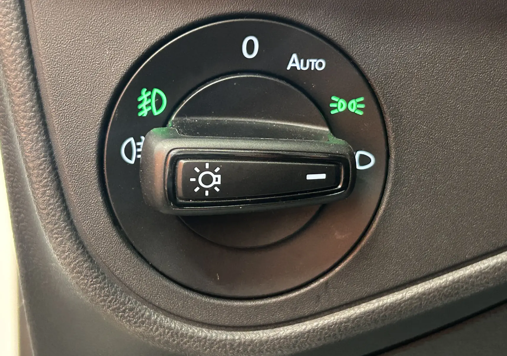 Gros plan sur le bouton de commande des phares du Volkswagen Taigo blanc, avec indicateurs lumineux verts allumés.
