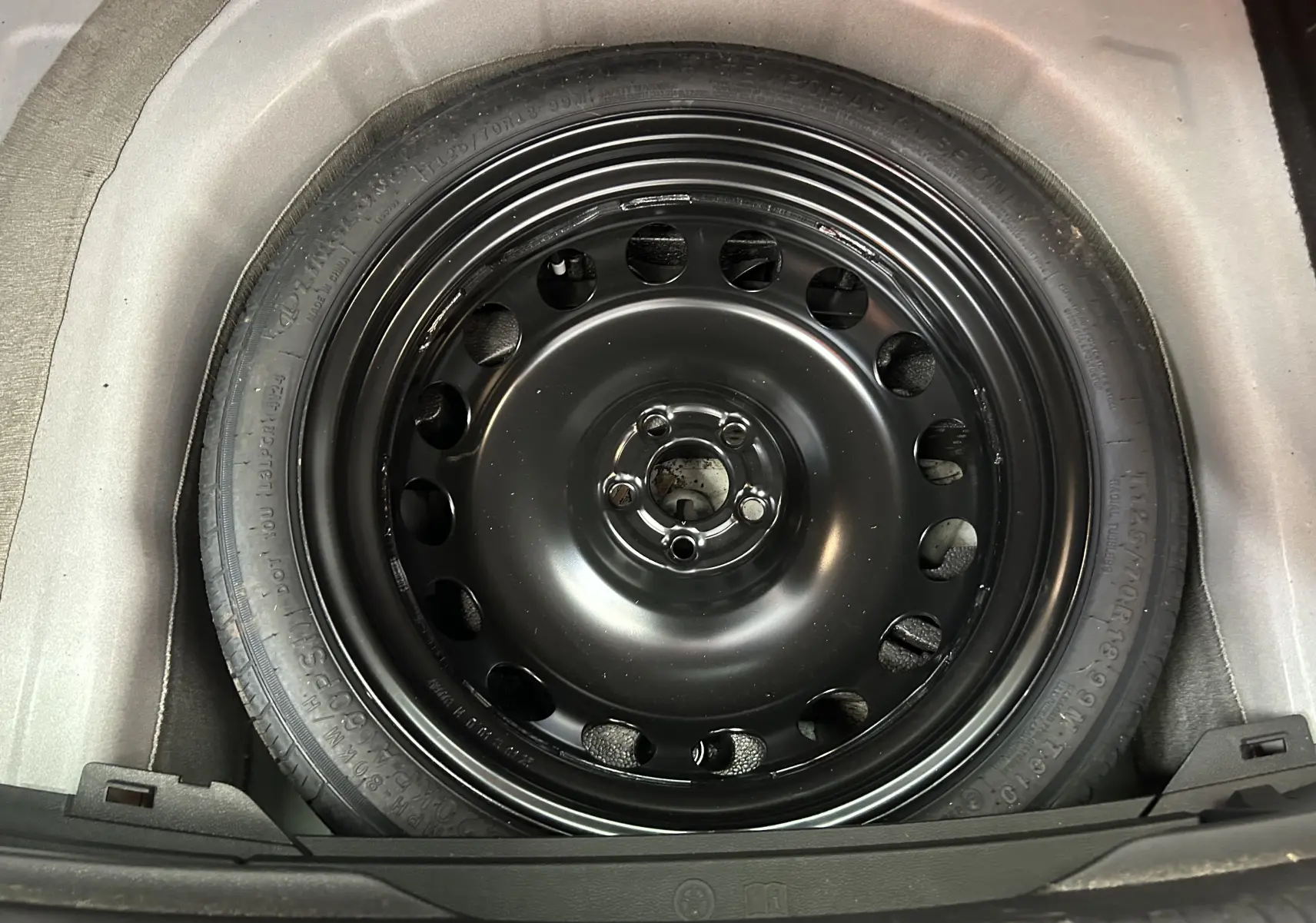 Gros plan sur la roue de secours noire en acier du coffre d'un Volkswagen Taigo blanc Pur TSI 110 DSG7 Style 2022.