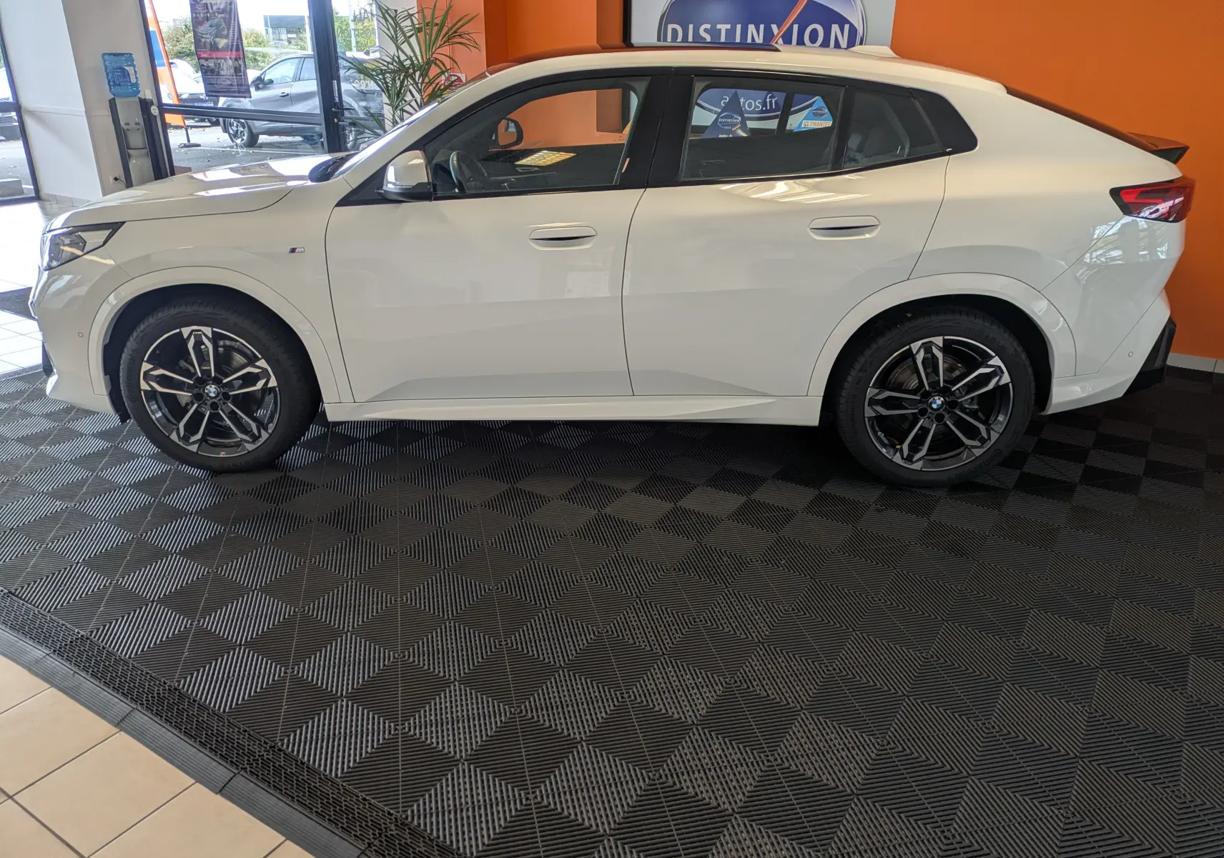 BMW X2 sDrive blanc alpin vu de 3/4 avant droit, avec jantes noires et toit panoramique en showroom.