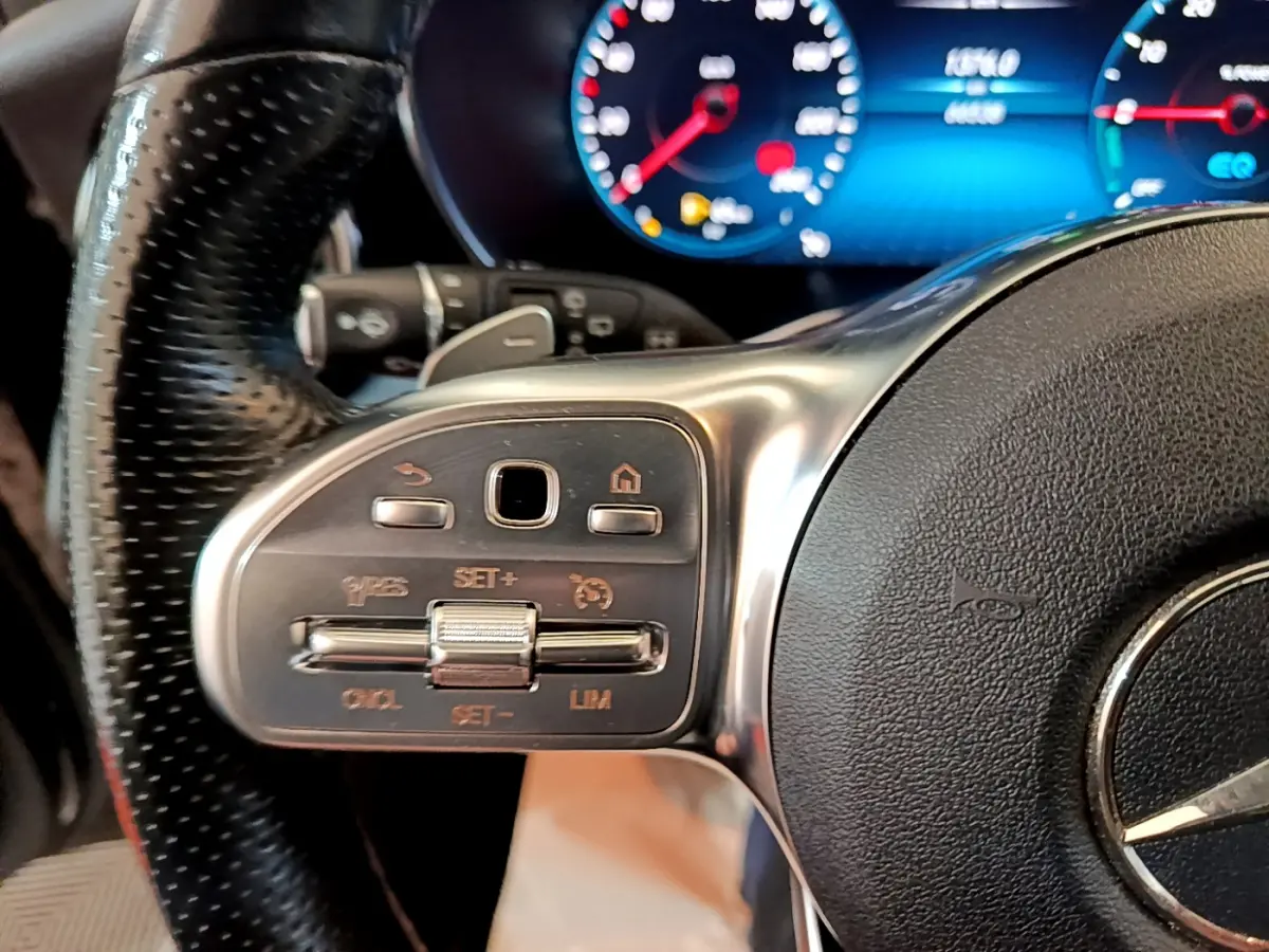 Gros plan sur les commandes à gauche du volant cuir noir du Mercedes GLC 300 E AMG Line 2021 avec tableau de bord numérique bleu.