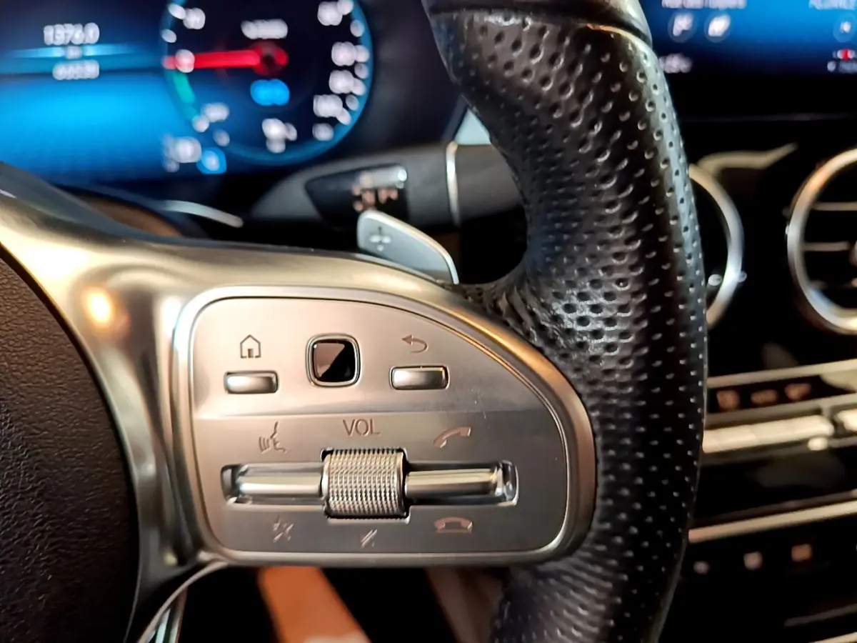 Gros plan sur les commandes du volant en cuir perforé du Mercedes GLC 300 E AMG Line 2021, avec tableau de bord numérique flou.