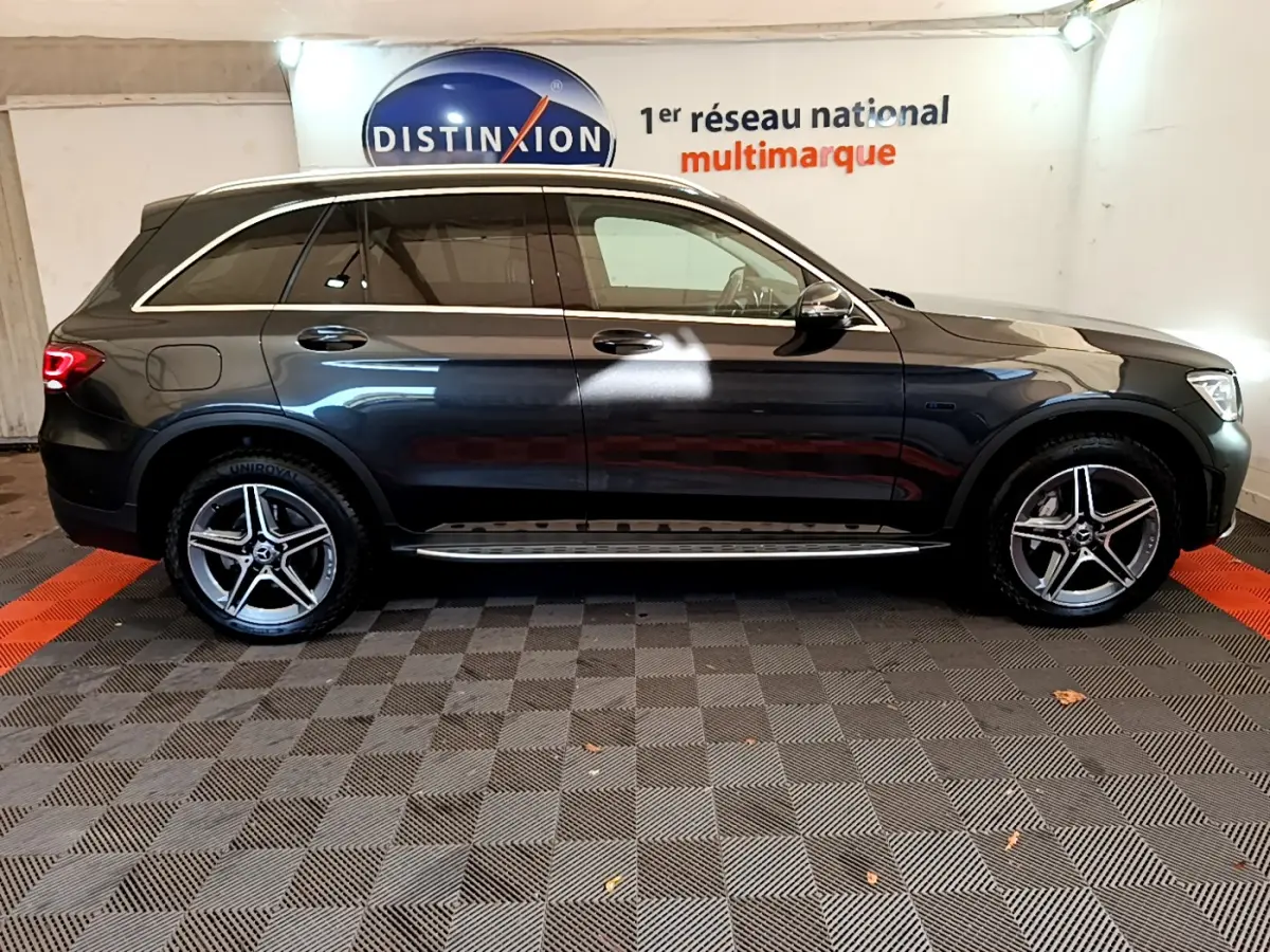 Profil côté droit d'un Mercedes GLC 300 E AMG Line gris foncé avec jantes alliage et vitres teintées en intérieur showroom.
