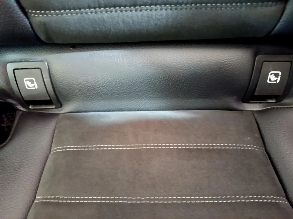 Gros plan sur la commande de rabattement des sièges arrière en cuir noir avec surpiqûres blanches dans un Mercedes GLC gris foncé.