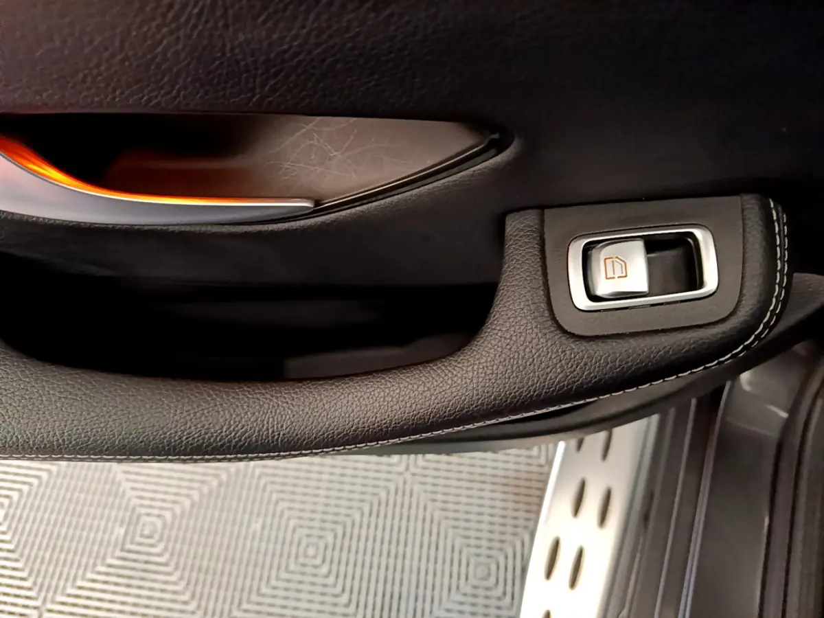 Gros plan sur la poignée intérieure noire et le bouton de lève-vitre du côté gauche d’un Mercedes GLC gris foncé.