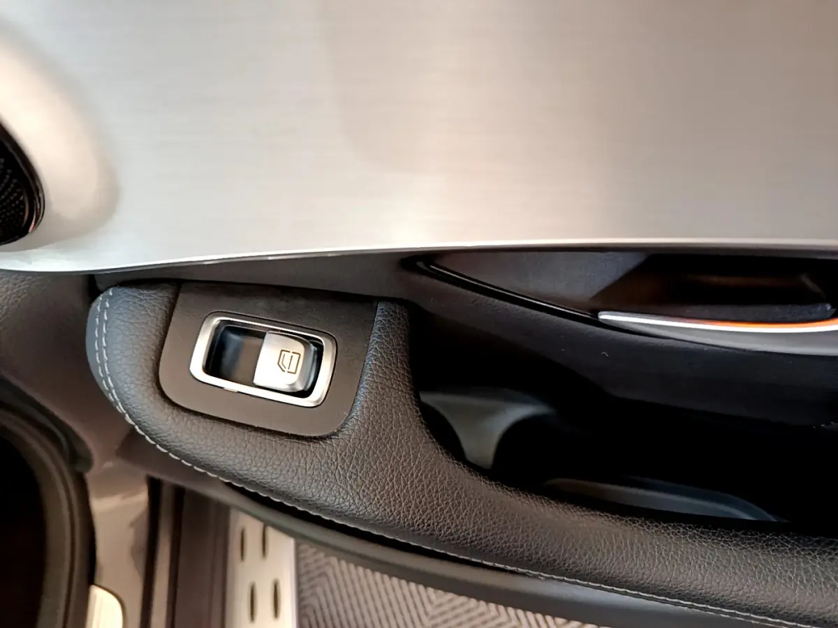 Gros plan sur la commande de lève-vitre en cuir noir et aluminium sur la portière côté conducteur du Mercedes GLC gris foncé.