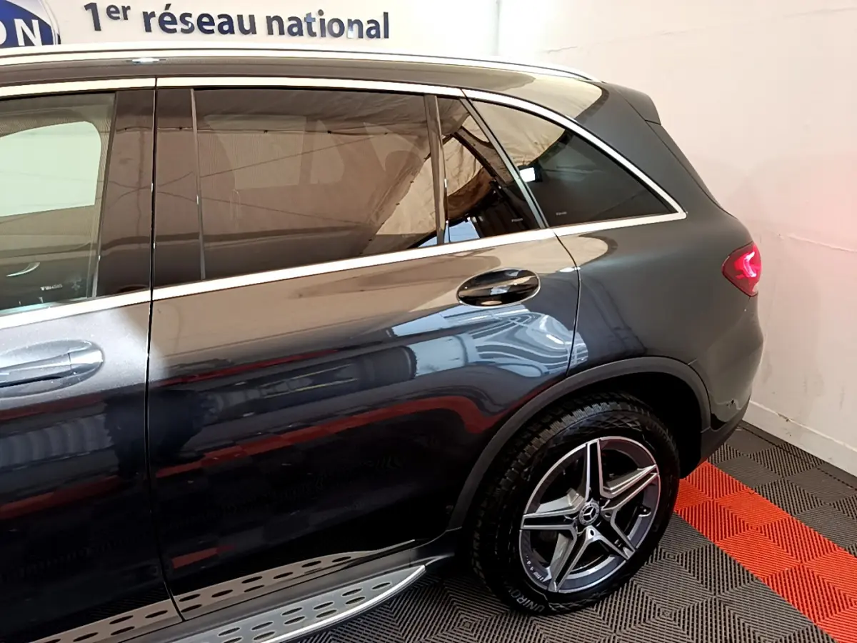 Vue latérale arrière droite d'un Mercedes GLC 300 E AMG Line gris foncé avec jantes alliage et feux arrière LED allumés.