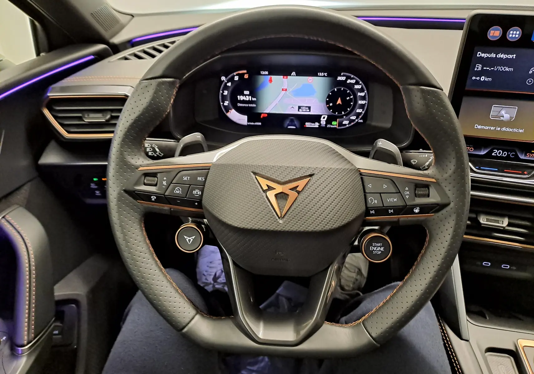 Vue rapprochée du volant perforé noir avec logo cuivré de la CUPRA LEON ST 2.0 TDI, tableau de bord digital en arrière-plan.