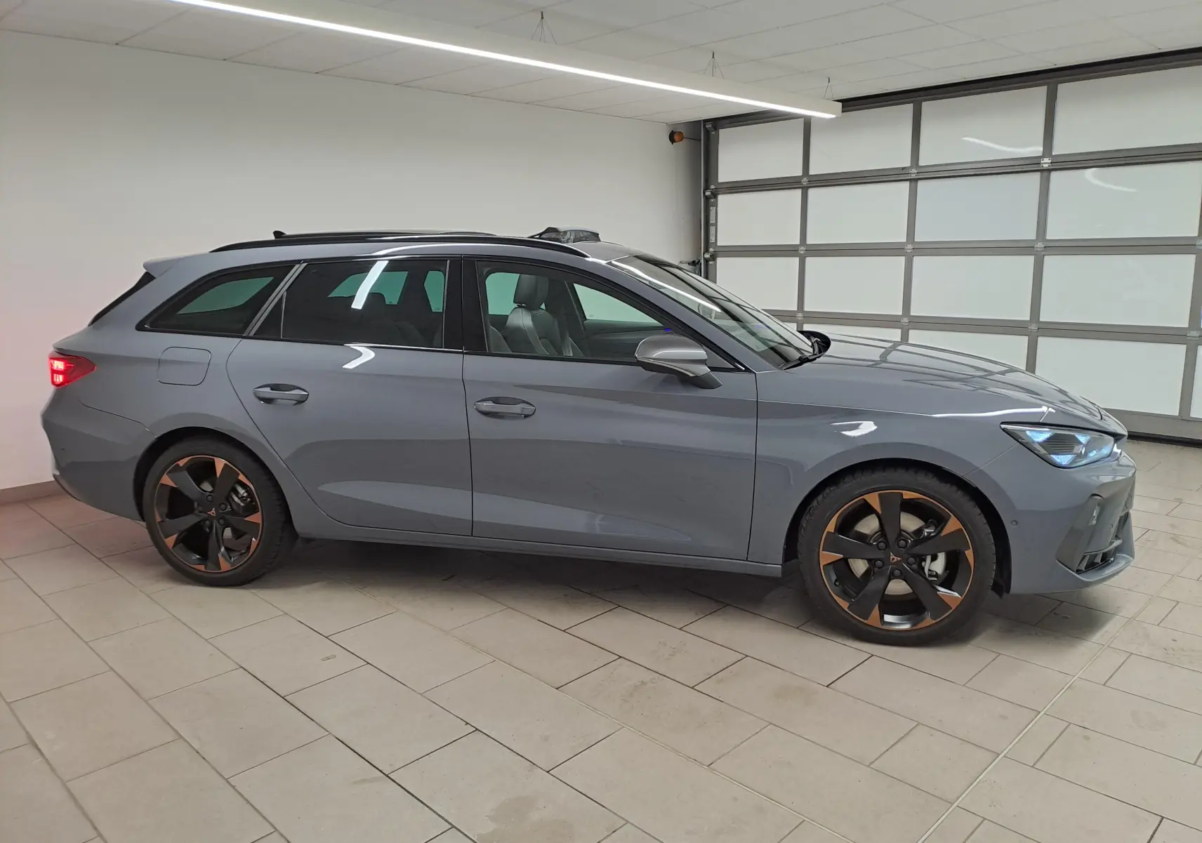 Vue de profil côté gauche d'une CUPRA Leon ST 2025 gris Graphène avec jantes cuivrées et toit ouvrant panoramique.