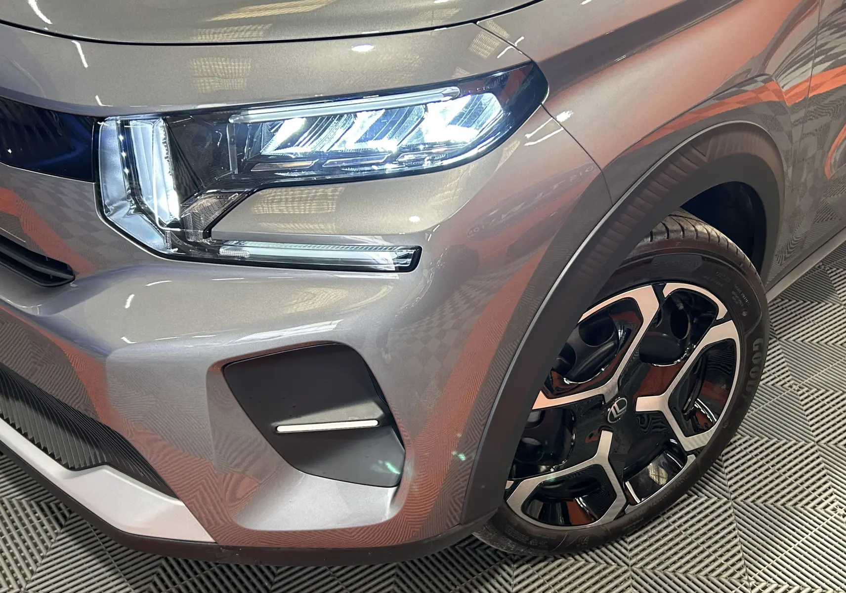 Gros plan sur l'avant droit gris Artense de la Citroën C3 2025, mettant en valeur le phare LED et la jante noire et argent.