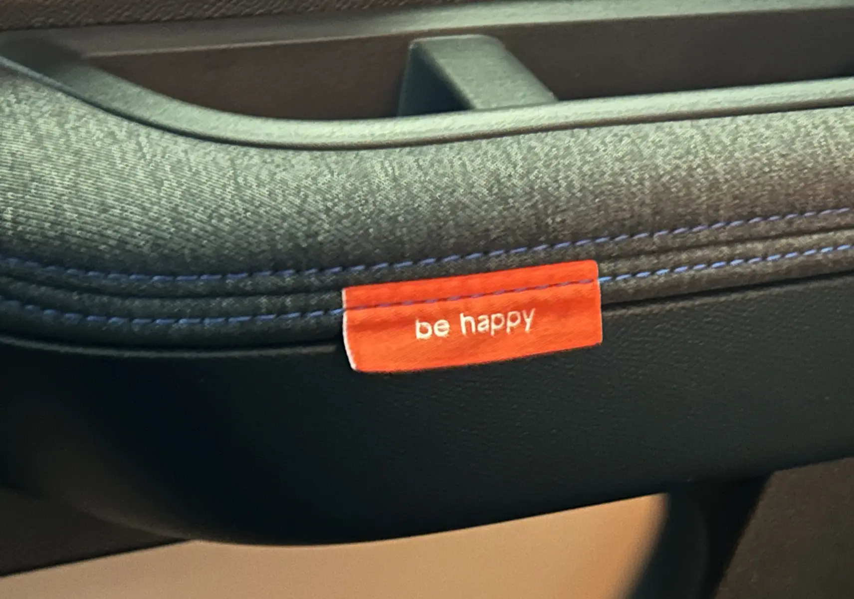 Gros plan sur la poignée de porte intérieure en tissu gris avec étiquette rouge "be happy" sur Citroën C3 2025.