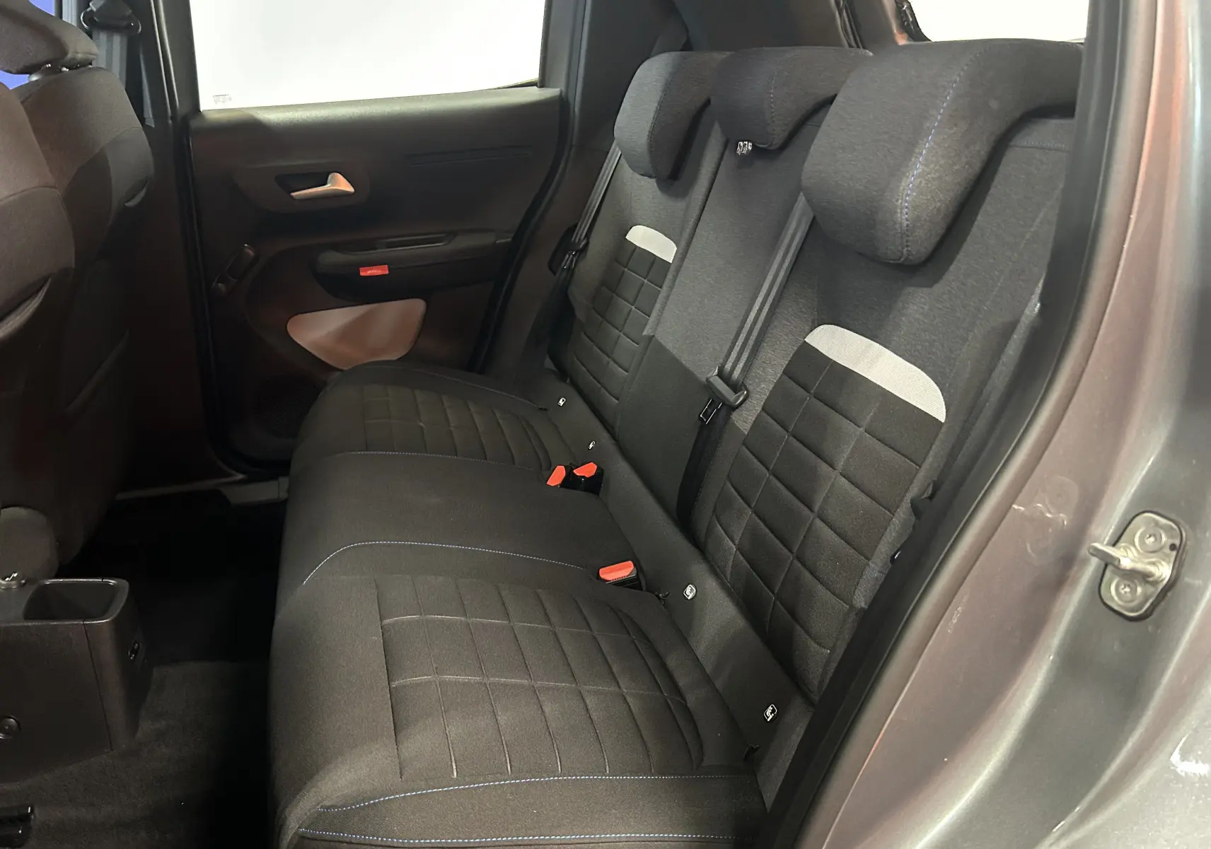 Vue intérieure côté arrière droit montrant les sièges arrière en tissu noir avec surpiqûres bleues de la Citroën C3 Gris Artense.