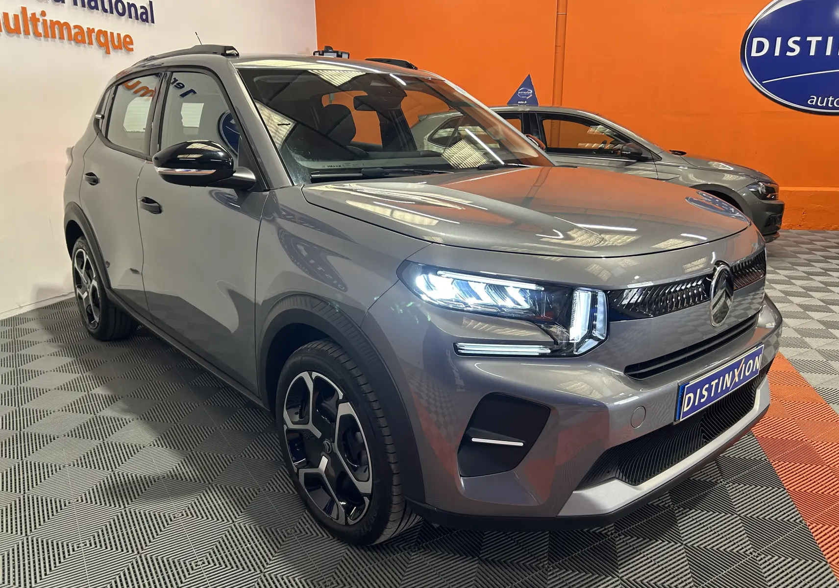 Vue 3/4 avant d'une Citroën C3 Turbo 100 PLUS gris Artense avec phares LED allumés dans un showroom.