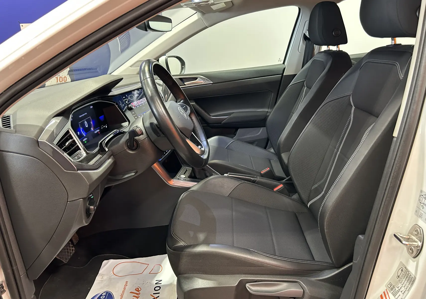 Vue intérieure côté conducteur du Volkswagen Taigo blanc, montrant les sièges noirs et le tableau de bord numérique moderne.