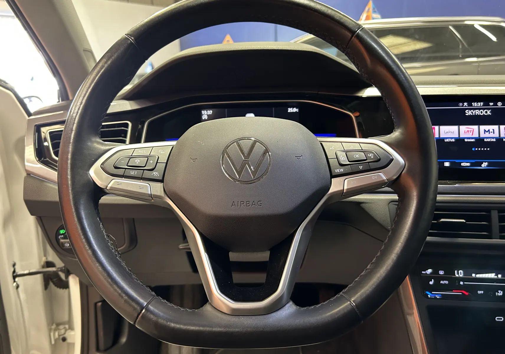 Vue rapprochée du volant en cuir noir du Volkswagen Taigo blanc, avec commandes intégrées et tableau de bord numérique visible.