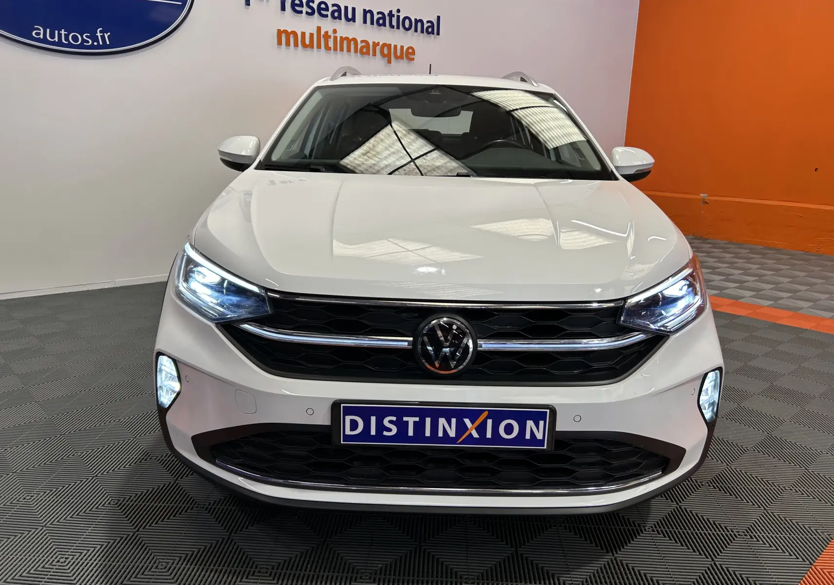 Vue frontale d'un Volkswagen Taigo TSI 110 DSG7 Style blanc pur avec phares LED allumés en intérieur showroom.