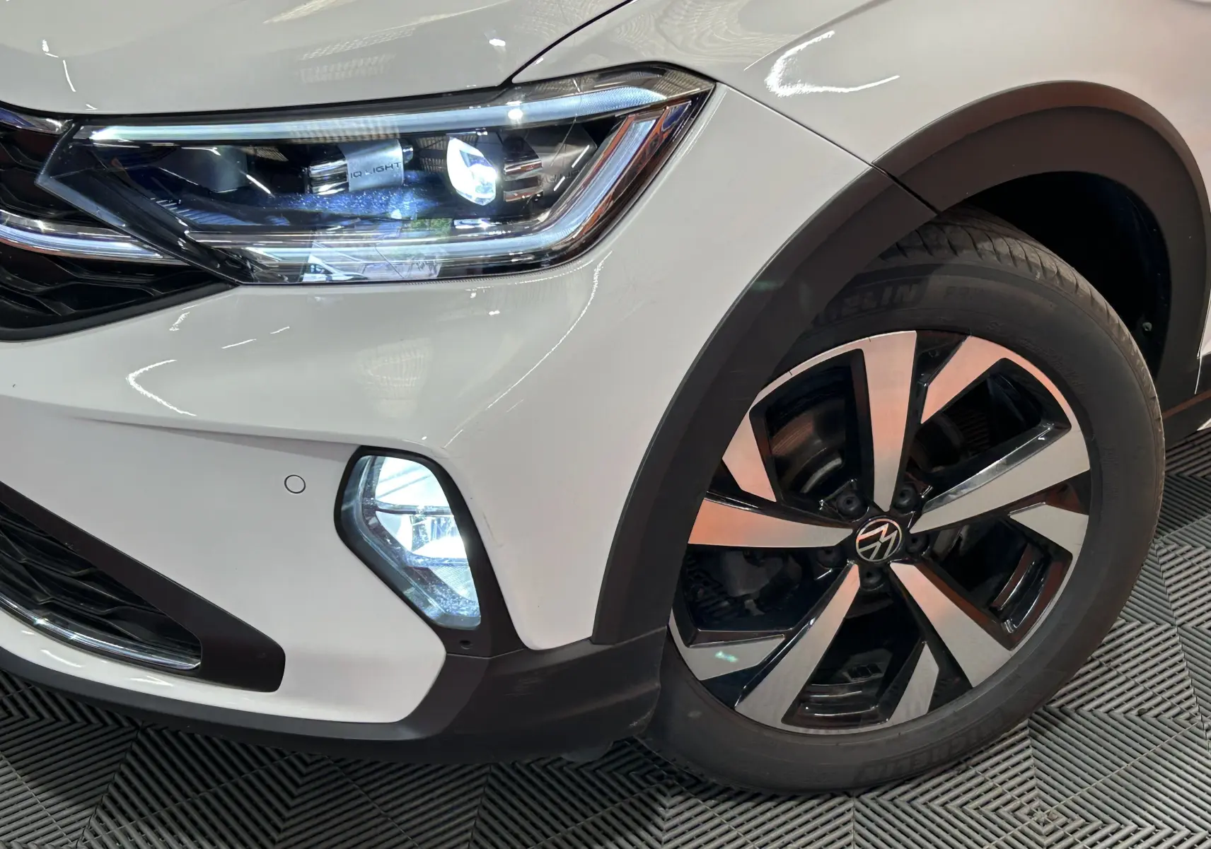 Gros plan sur l'avant droit blanc pur du Volkswagen Taigo 2022, mettant en valeur le phare LED et la jante alliage bicolore.