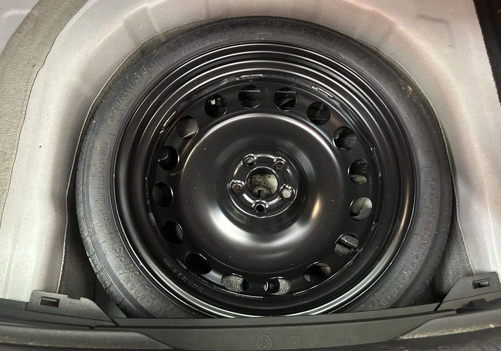 Roue de secours noire en acier du Volkswagen Taigo TSI 110 DSG7 Style 2022, vue en plongée dans le coffre.