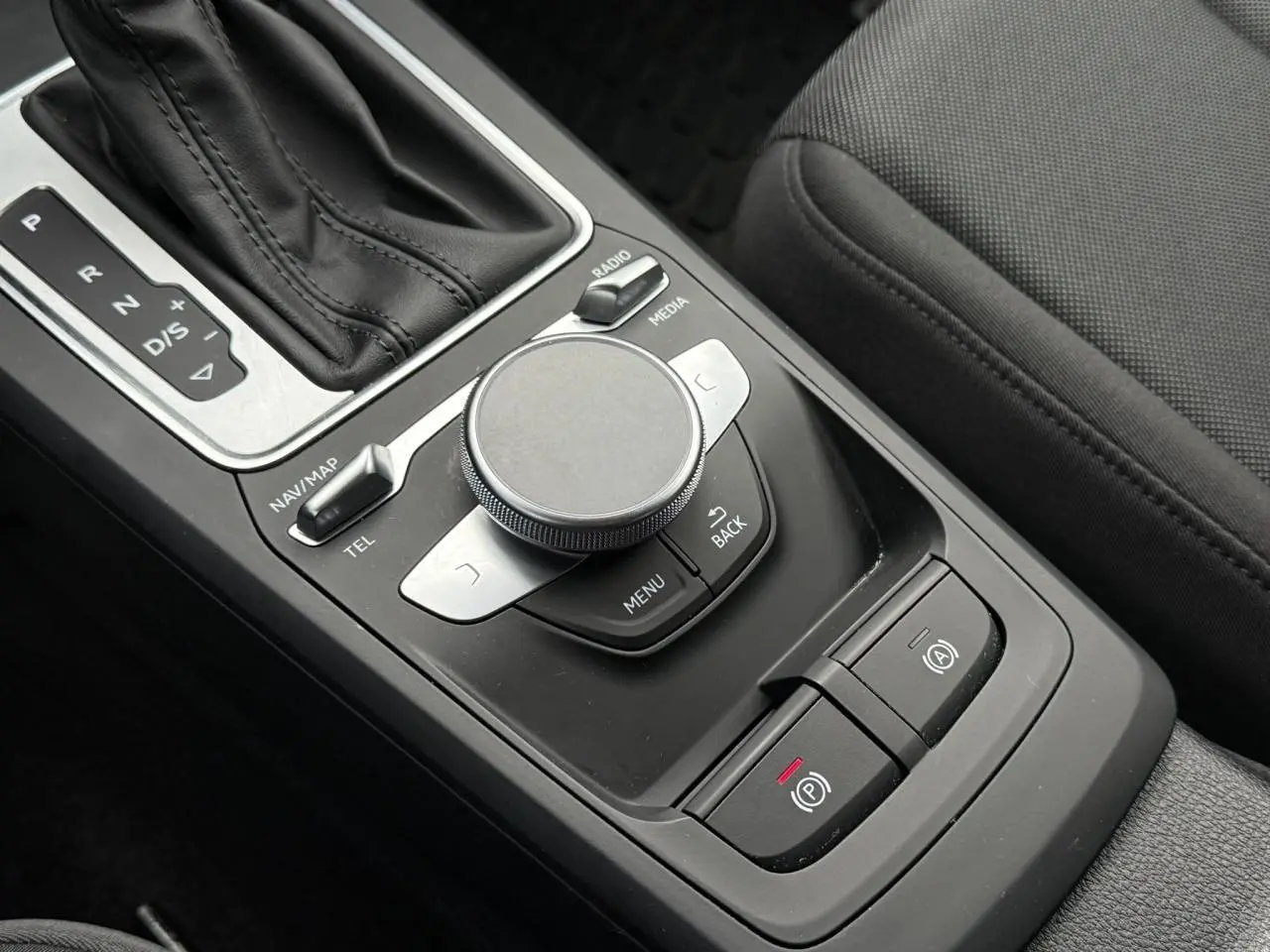 Gros plan sur la console centrale noire de l'Audi Q2 35 TFSI S-Line, montrant la molette MMI et le levier de vitesses automatique.