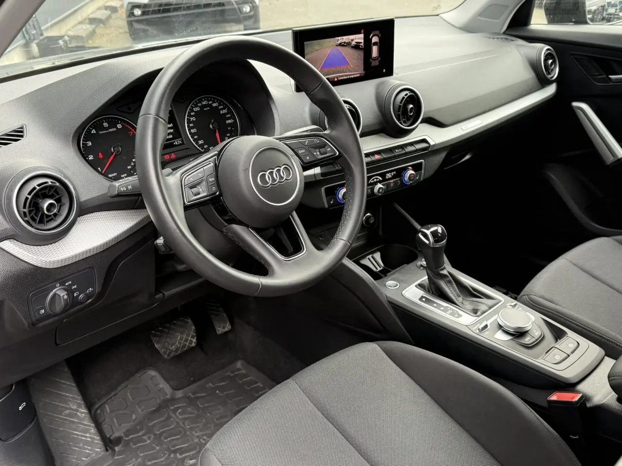 Intérieur noir de l'Audi Q2 35 TFSI 2023 vu côté conducteur, avec tableau de bord et écran caméra de recul.