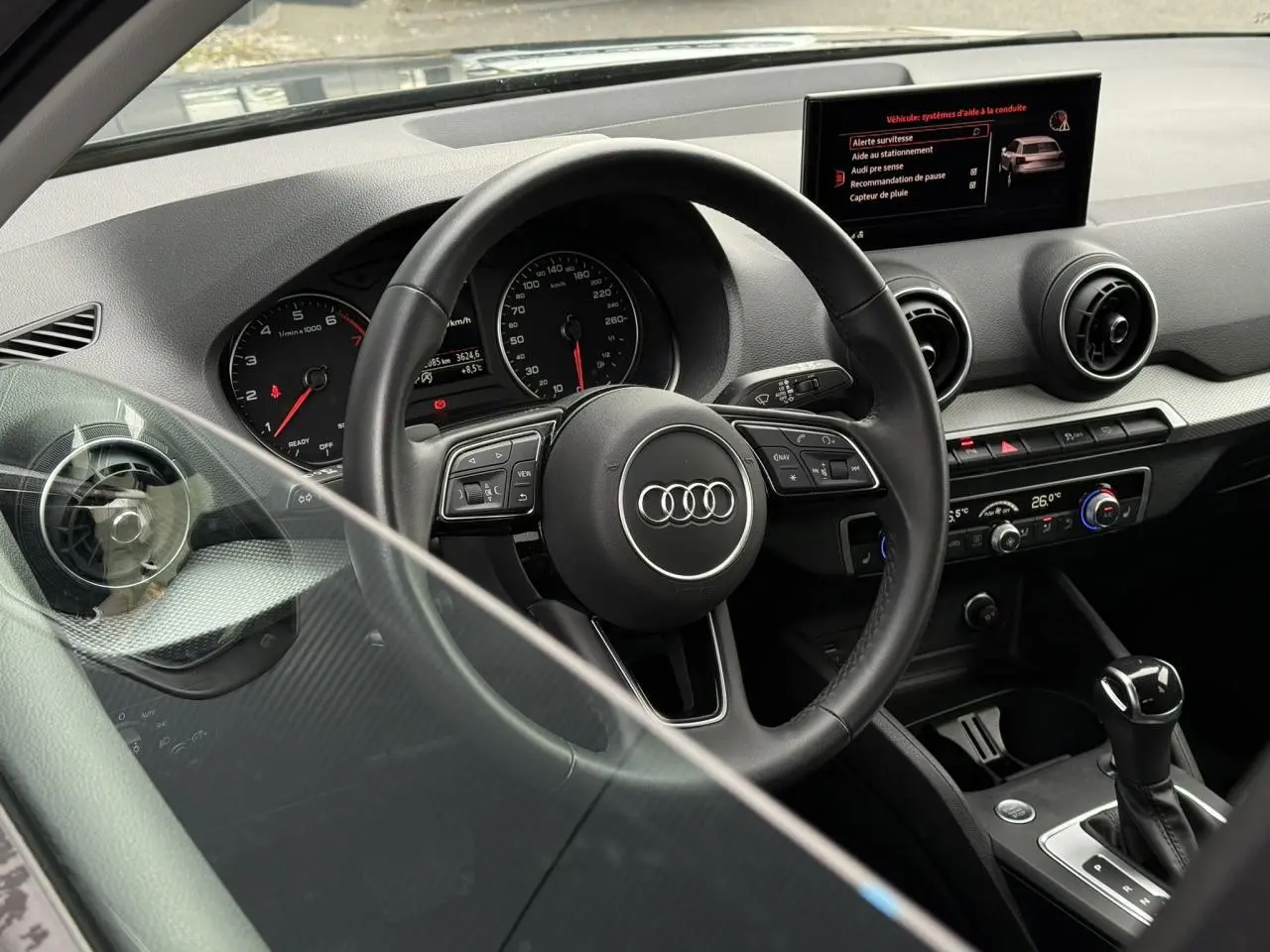 Intérieur de l'Audi Q2 35 TFSI S-Line 2023, vue du poste de conduite avec volant multifonction et écran central.