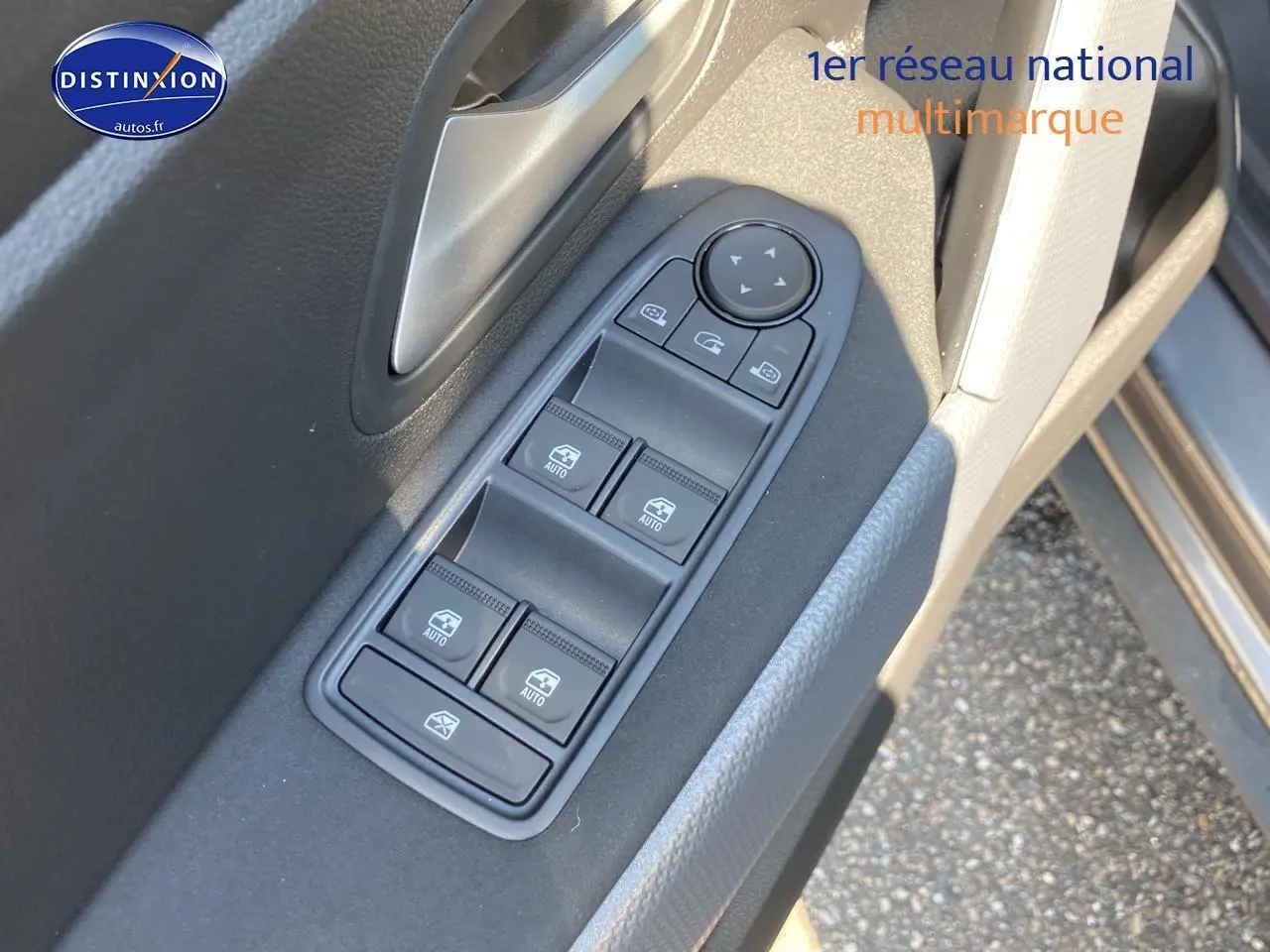 Gros plan sur la commande des vitres électriques côté gauche d’un Dacia Duster gris schiste, avec poignée argentée.