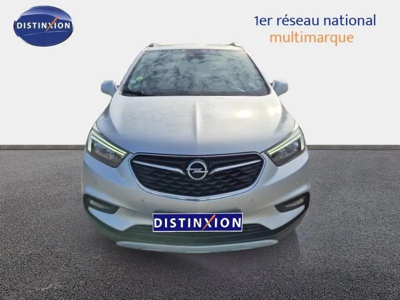 Vue avant d’un Opel Mokka X gris minéral avec calandre noire et feux LED allumés sur fond neutre.