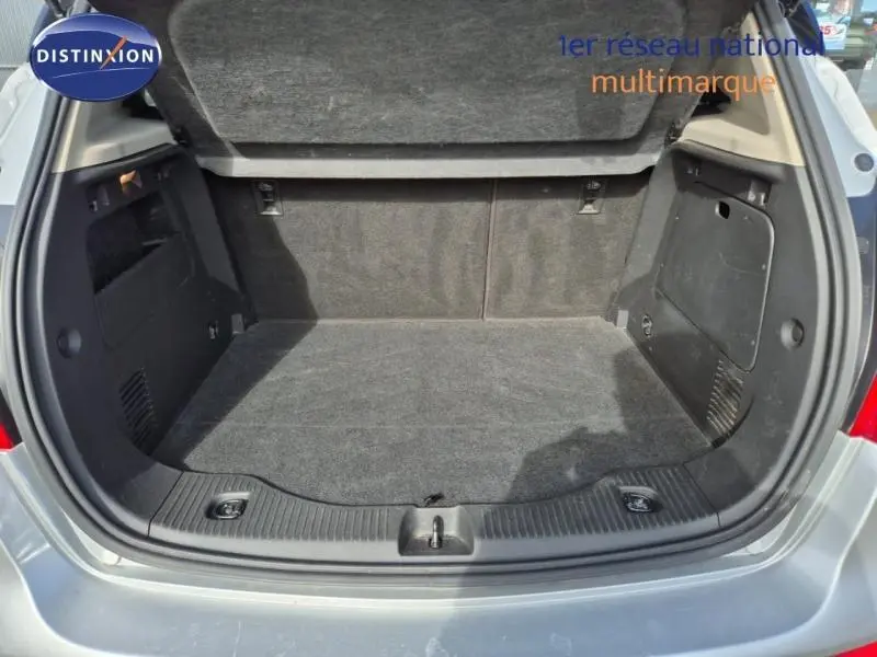 Coffre ouvert vu de l'arrière d'un Opel Mokka X gris minéral, montrant l'espace de chargement vide et doublé de moquette noire.