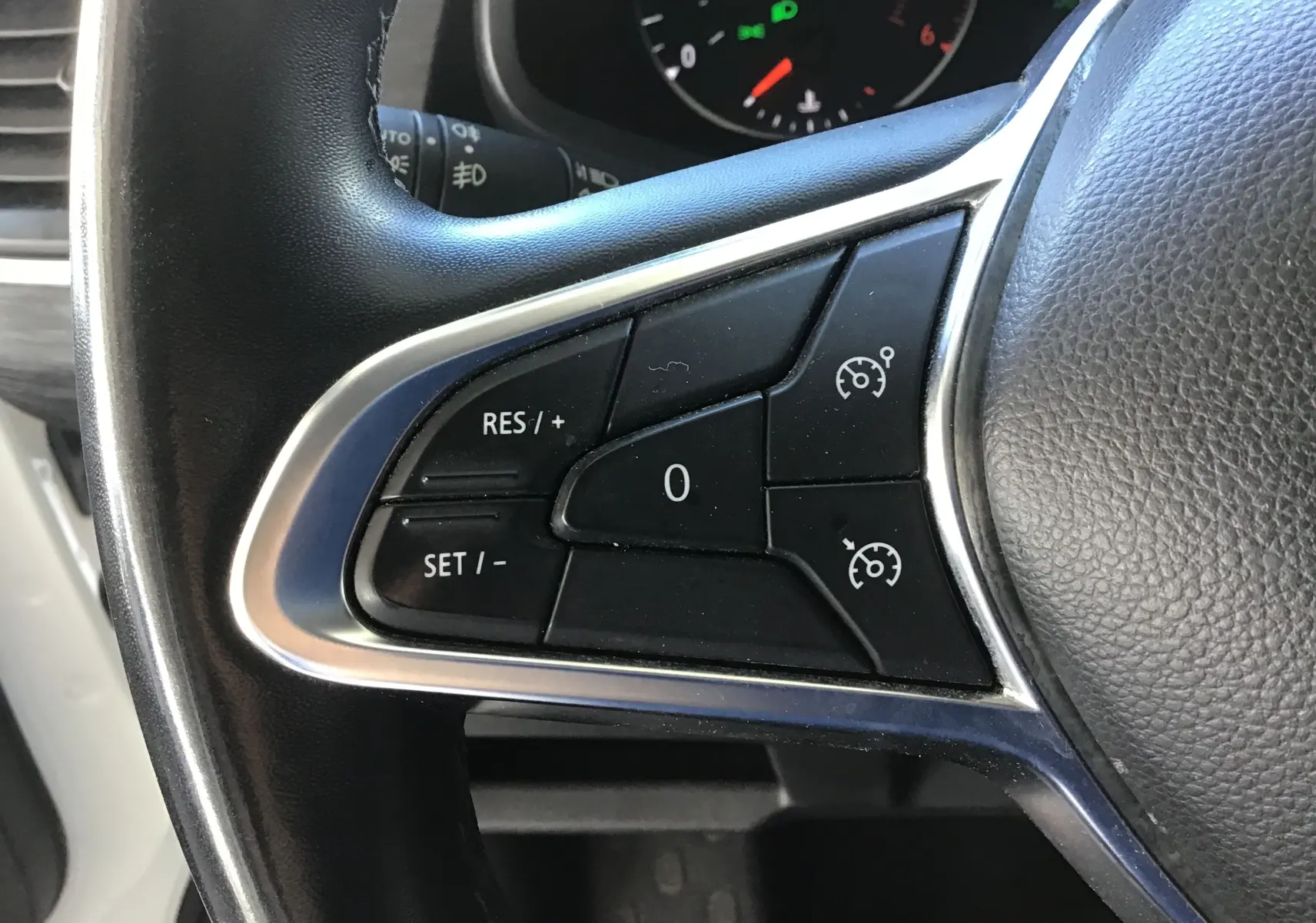 Gros plan sur les commandes de régulateur de vitesse au volant d'un Nissan Primastar blanc, tableau de bord en arrière-plan.