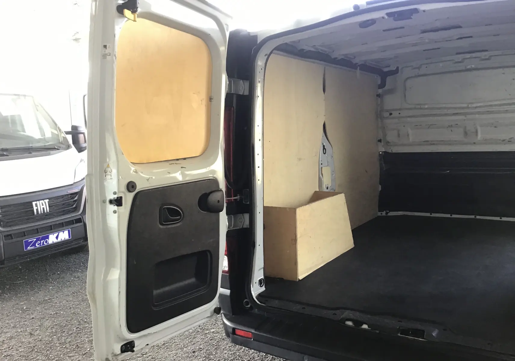 Vue arrière ouverte du fourgon blanc Nissan Primastar L1H1 montrant l'intérieur vide avec panneaux en bois.