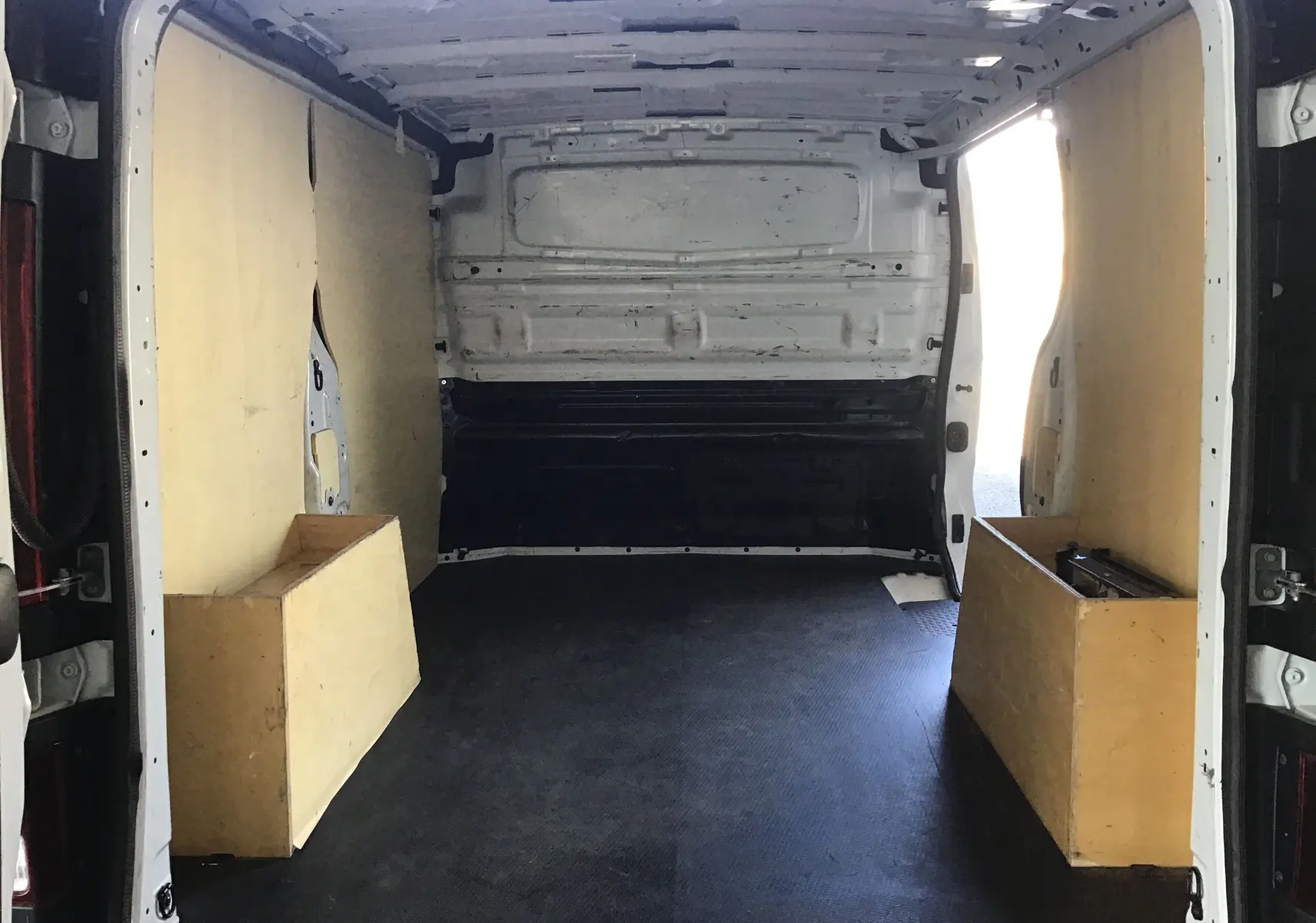 Vue intérieure arrière du fourgon blanc Nissan Primastar L1H1 2022 avec aménagements en bois sur les côtés du compartiment de chargement.