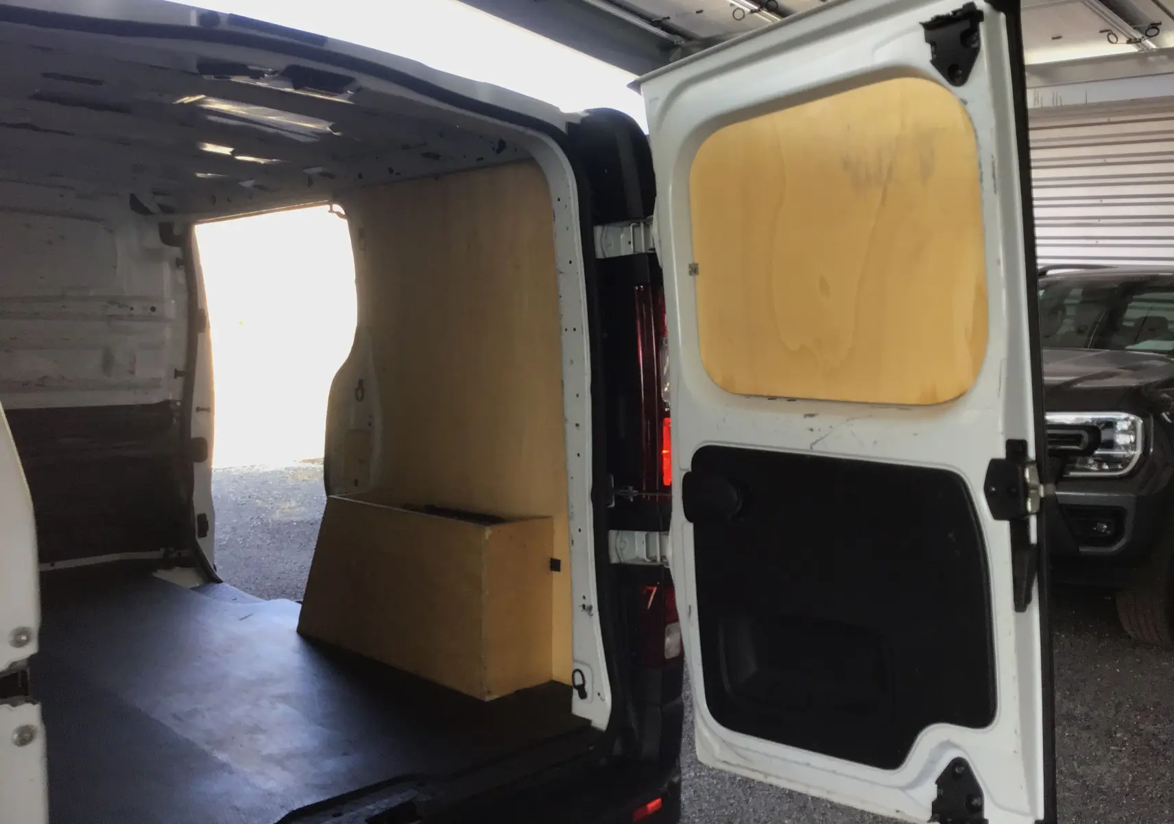 Vue arrière ouverte du fourgon blanc Nissan Primastar L1H1 2022, montrant l'intérieur avec panneaux en bois.