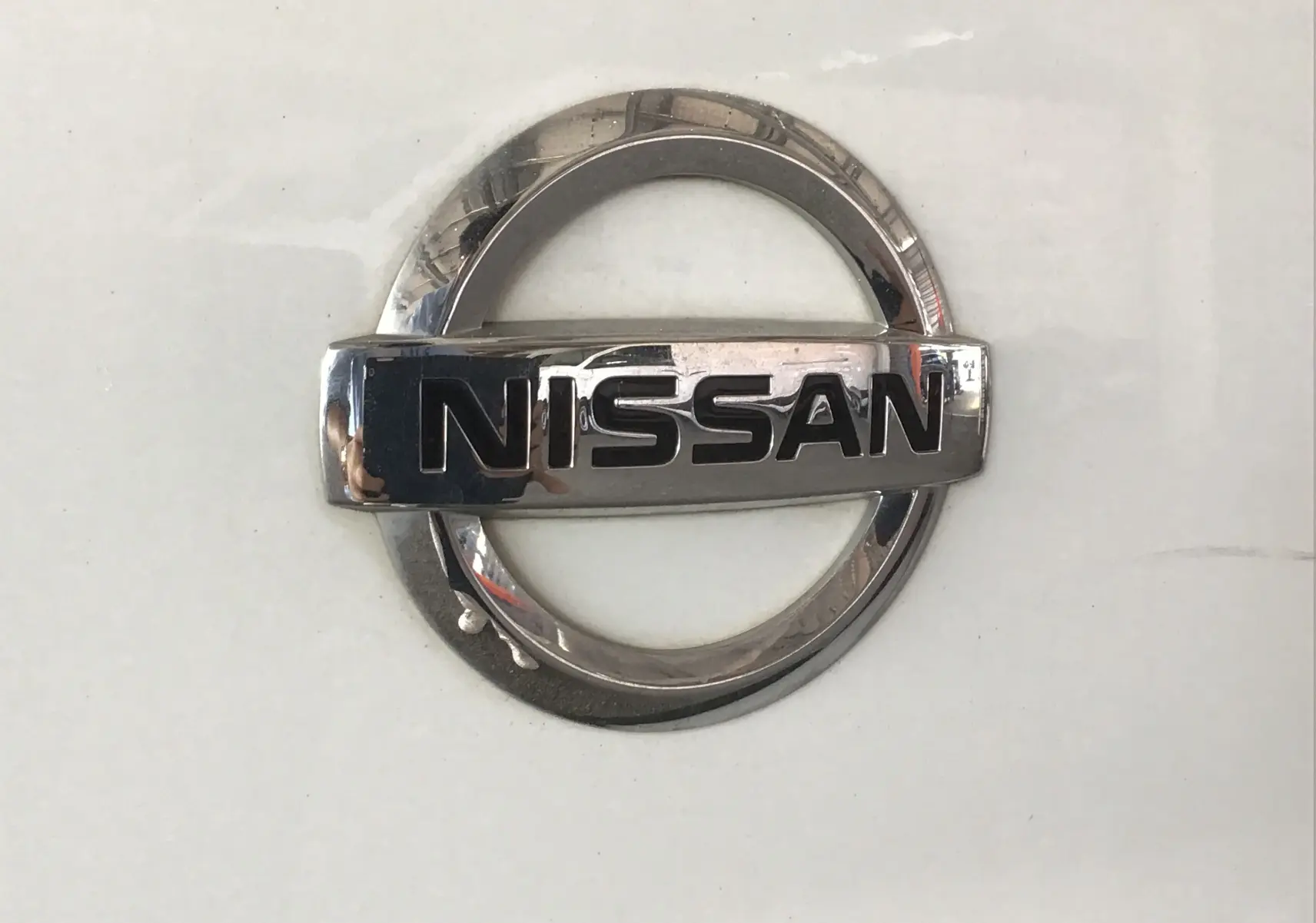Gros plan sur l'emblème chromé Nissan sur fond blanc du fourgon Primastar L1H1 2022.