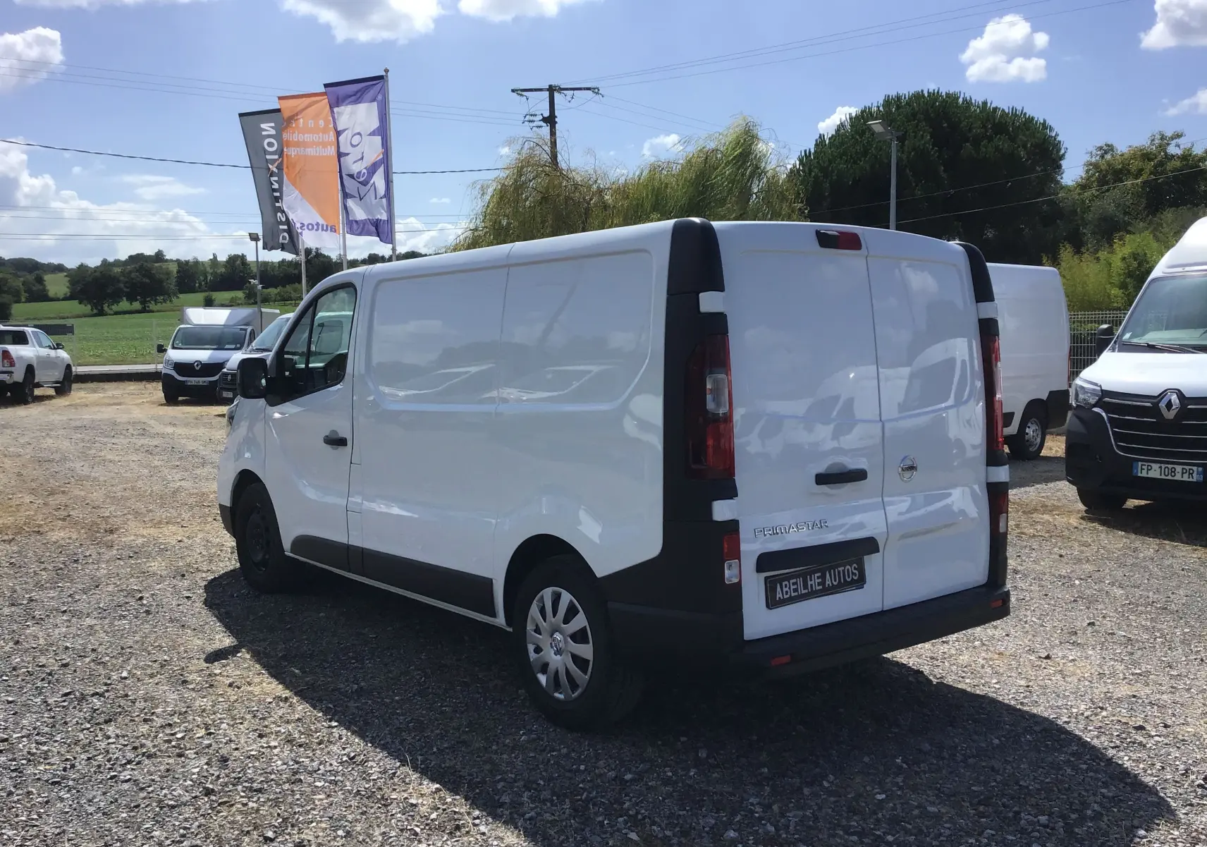 Vue 3/4 arrière droite d'un utilitaire blanc Nissan Primastar Fourgon L1H1 avec plaques Abeilhe Autos.