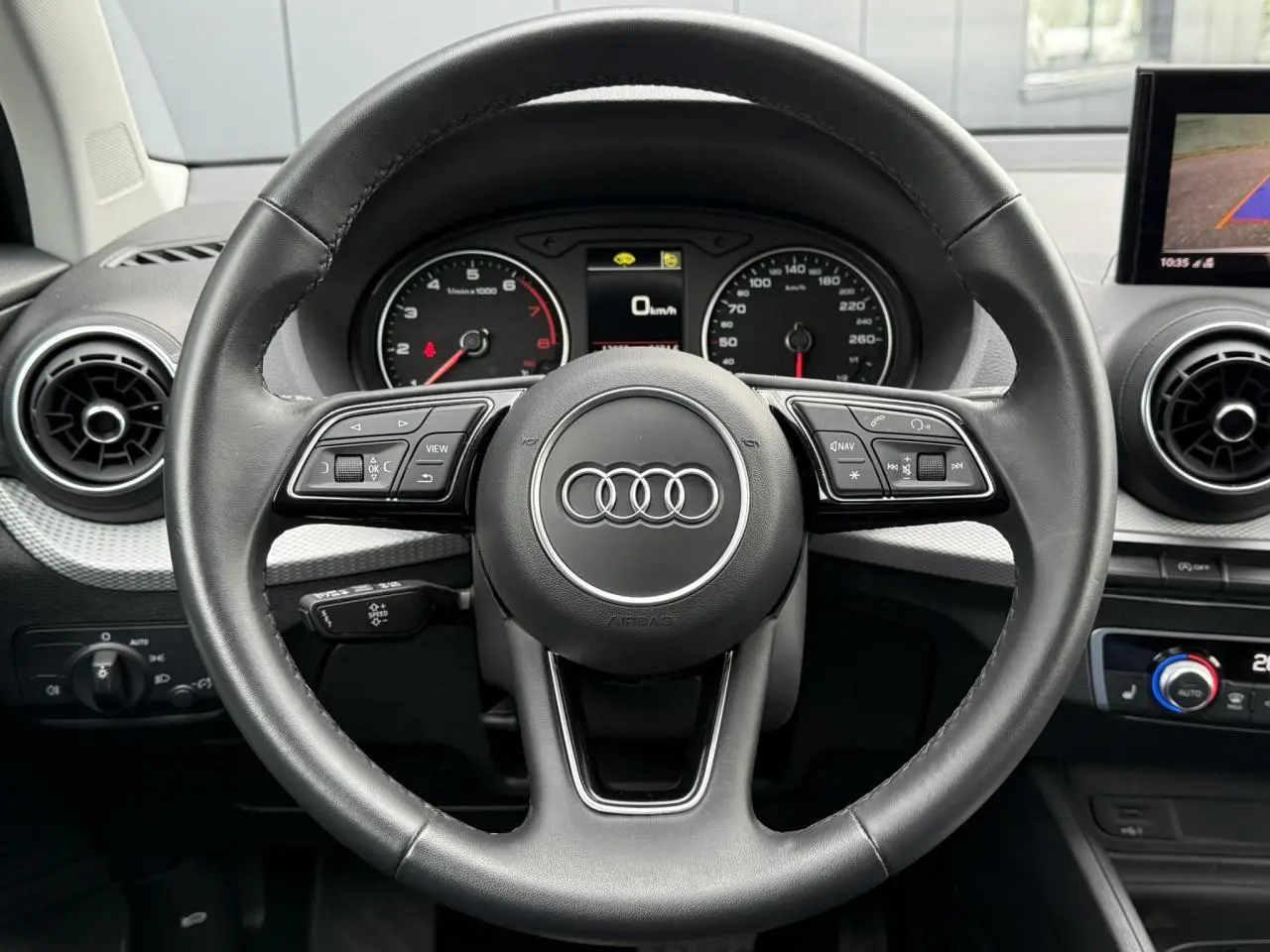Vue rapprochée du volant noir de l'Audi Q2 35 TFSI S-Line 2023 avec commandes intégrées et tableau de bord numérique.