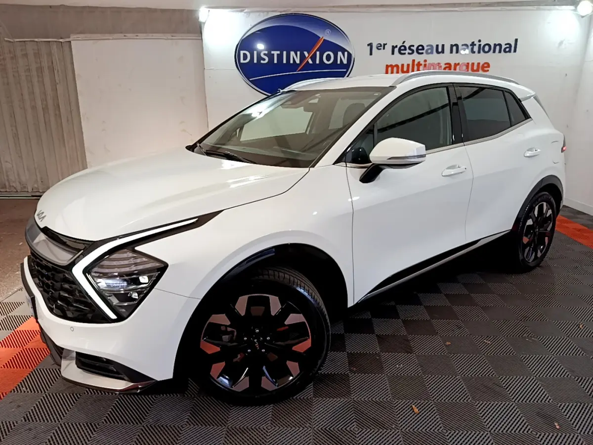 KIA SPORTAGE blanc en 3/4 avant droit, mettant en valeur ses phares LED en forme de flèche et ses jantes noires distinctives.