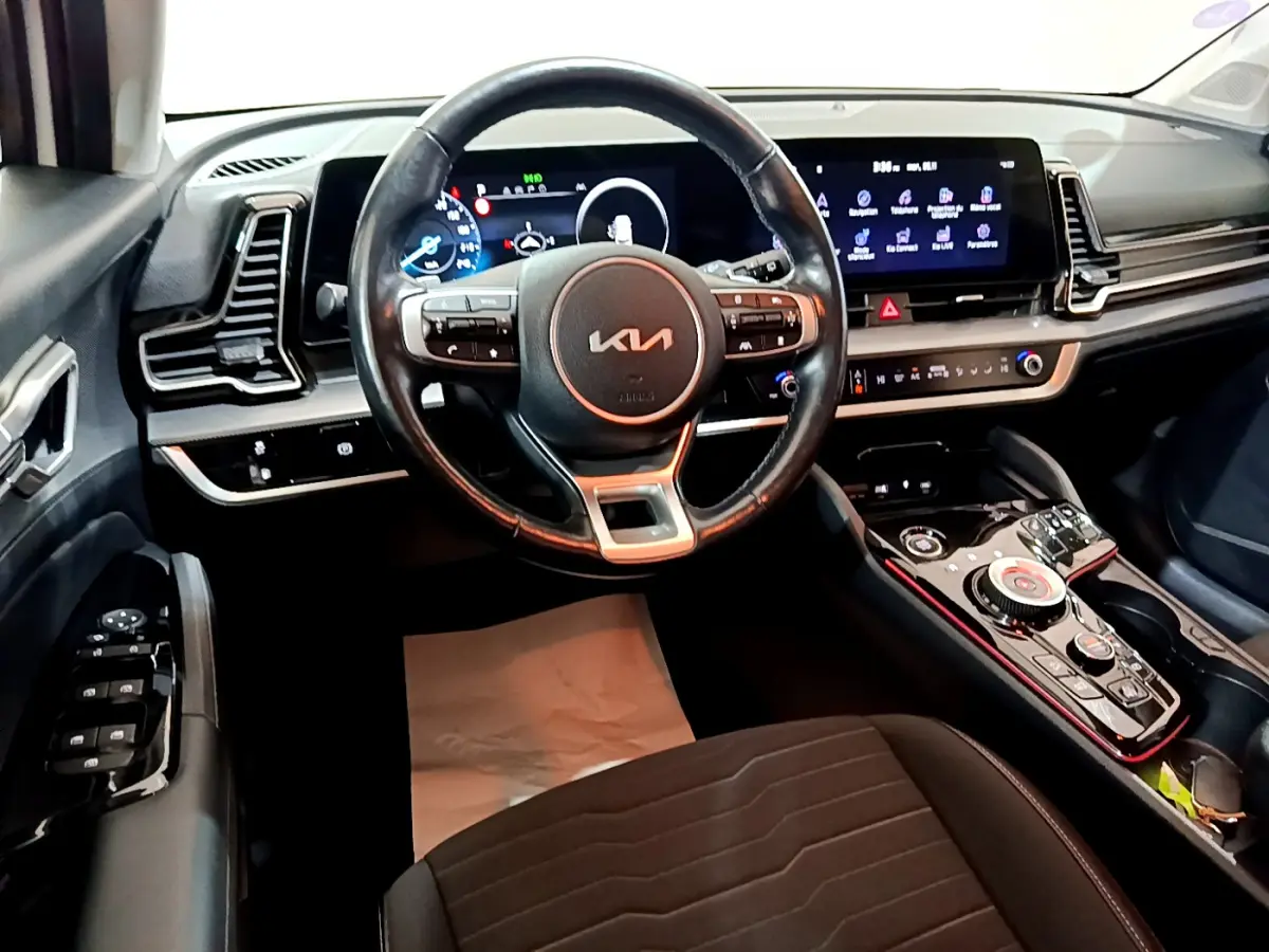 Vue intérieure avant du KIA SPORTAGE 2022 avec volant cuir, tableau de bord numérique et console centrale high-tech noire.