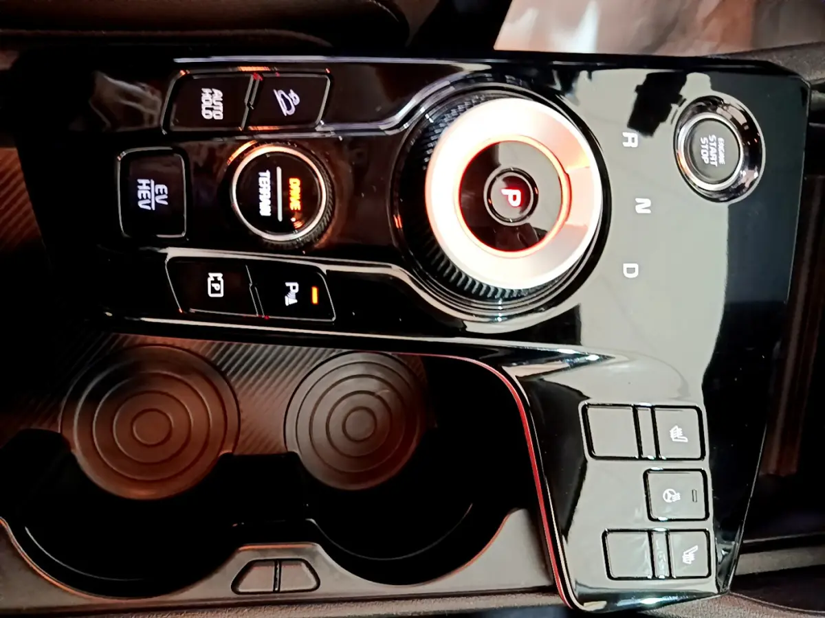 Gros plan sur la console centrale noire brillante du Kia Sportage hybride rechargeable 2022 avec molette de sélection et boutons lumineux.