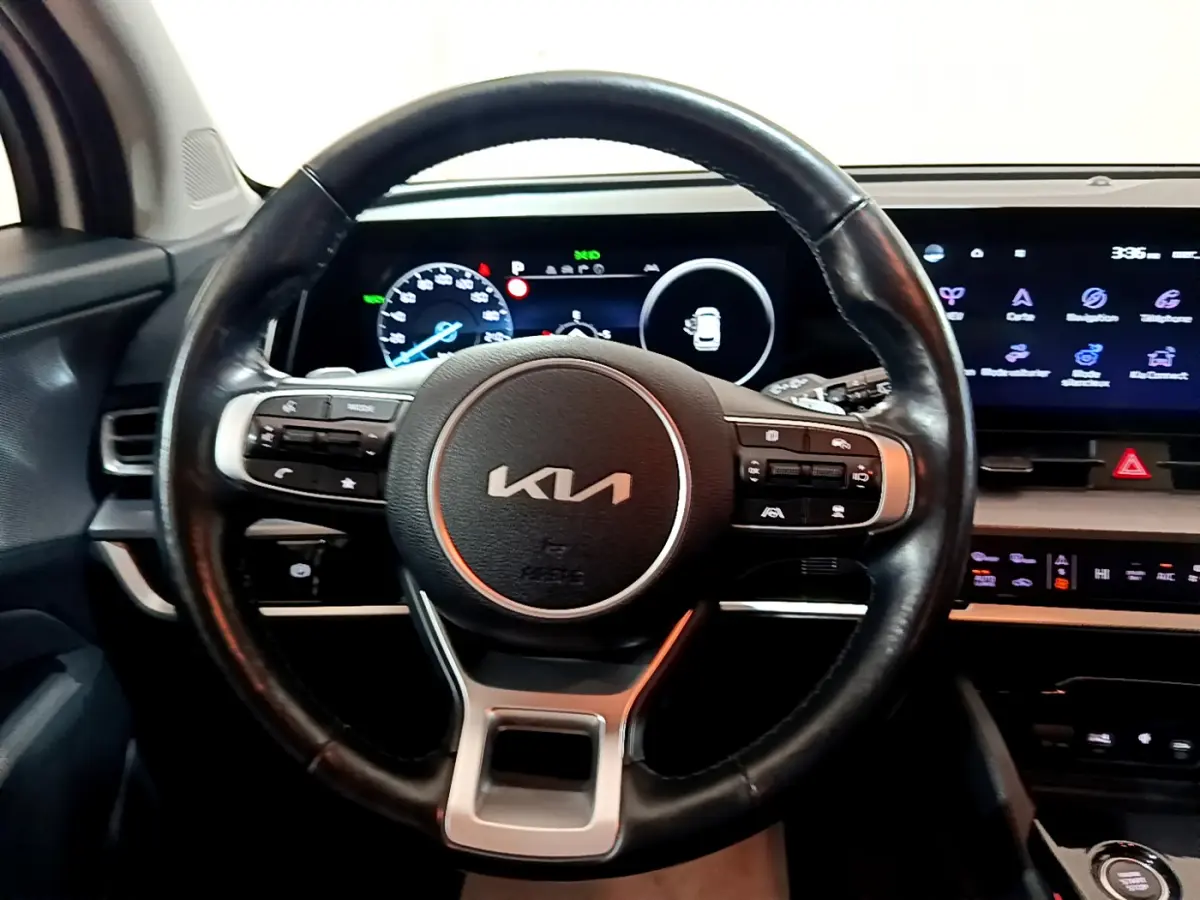 Vue intérieure centrée sur le volant cuir noir du Kia Sportage 2022 avec tableau de bord numérique et écran tactile.