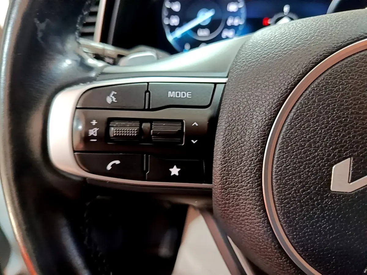 Gros plan sur les commandes gauche du volant cuir noir du Kia Sportage blanc 2022 avec affichage digital en arrière-plan.