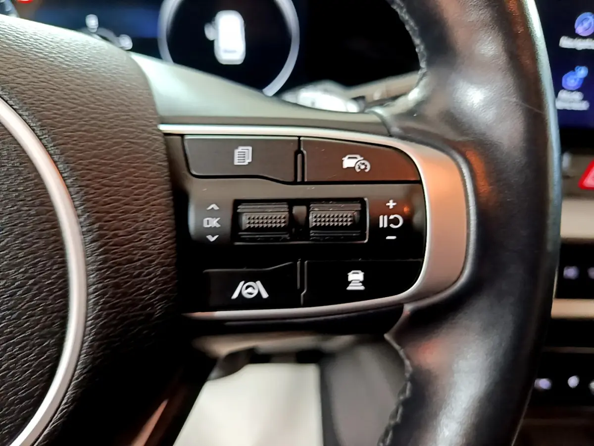 Gros plan sur les commandes du volant côté droit du Kia Sportage blanc hybride rechargeable 2022, boutons multifonctions visibles.