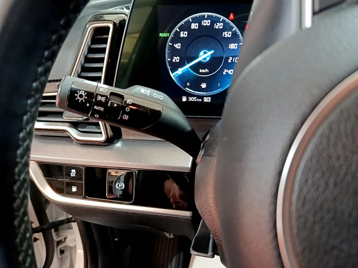 Gros plan sur le tableau de bord et volant du Kia Sportage hybride blanc, affichage numérique et commandes lumineuses visibles.