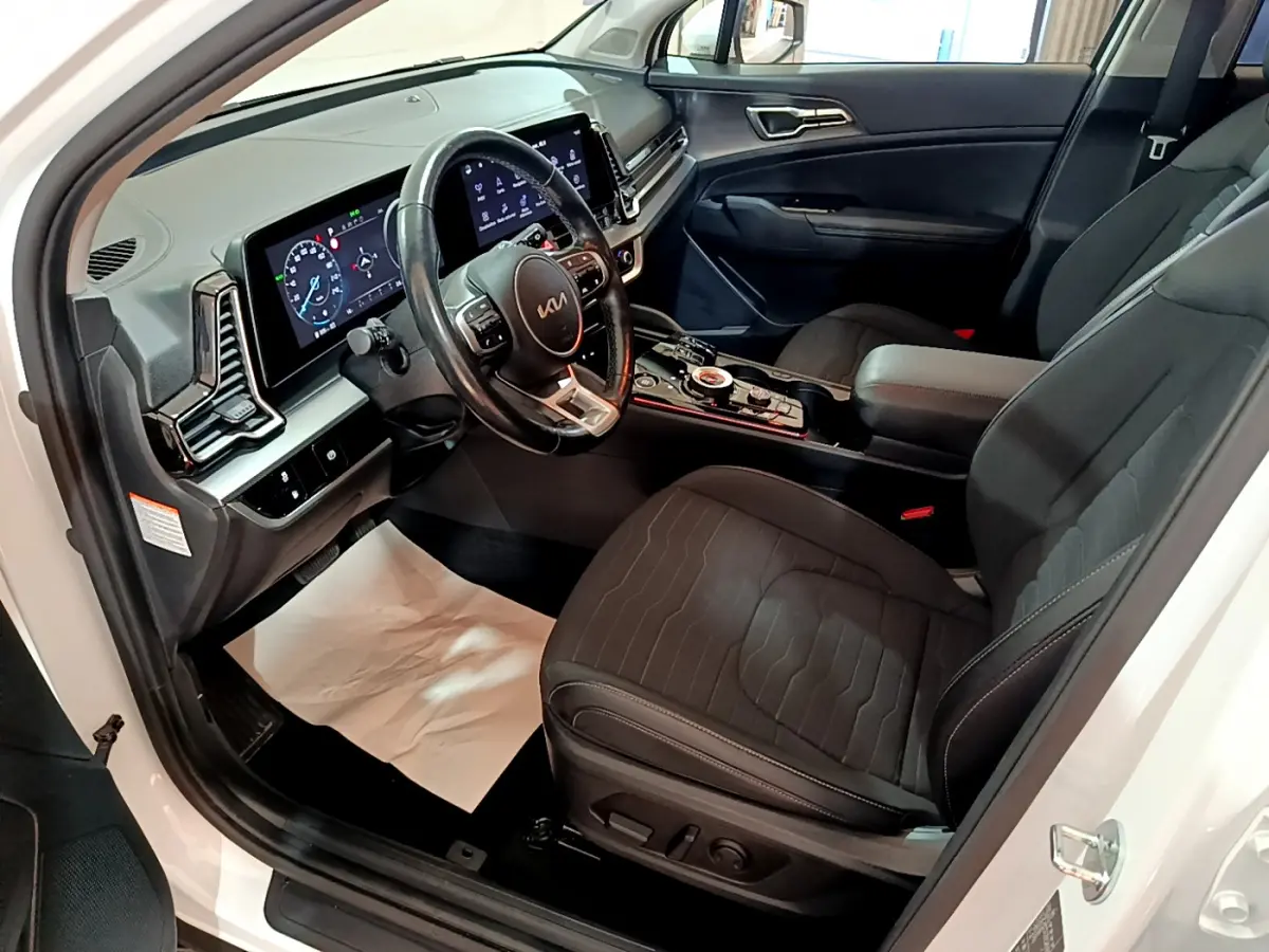 Intérieur avant droit du KIA SPORTAGE blanc 2022, avec tableau de bord numérique et sièges noirs en tissu.