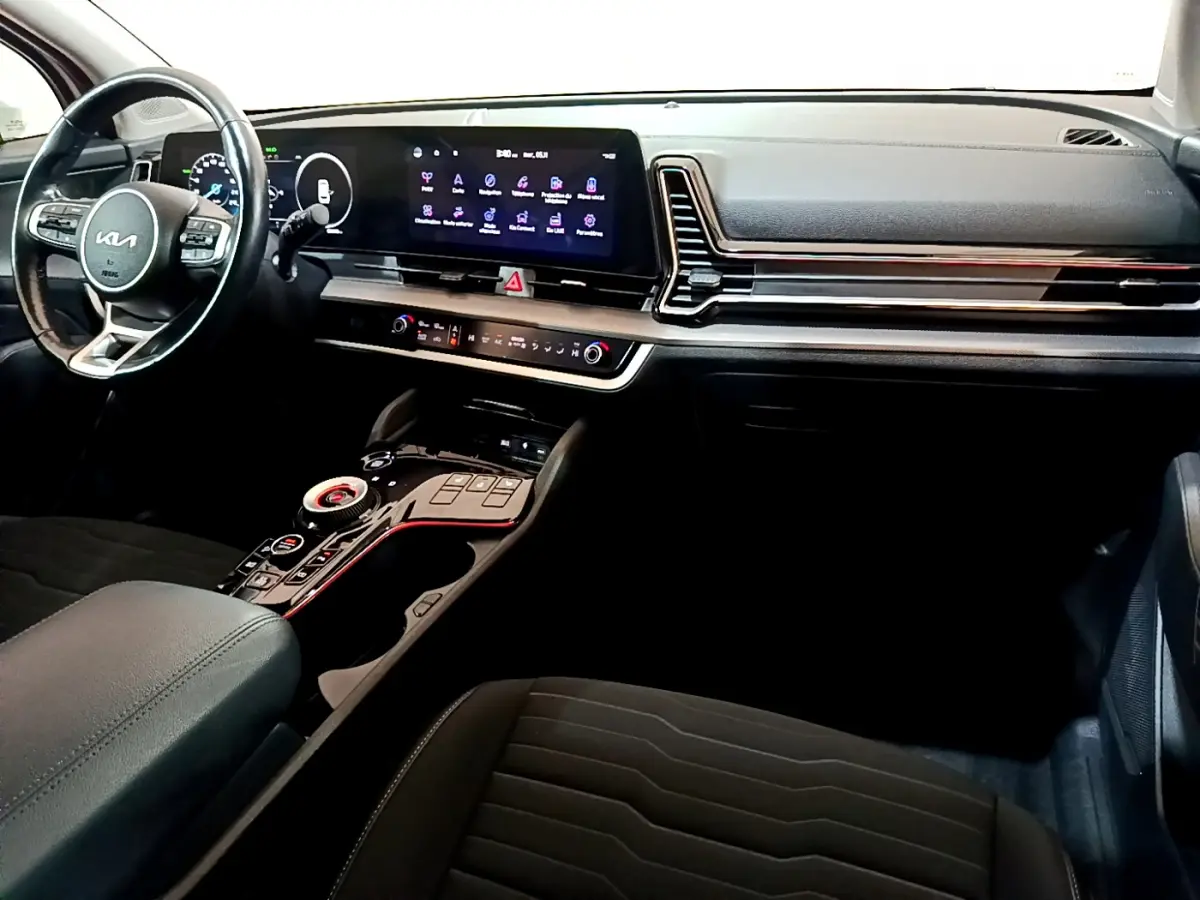 Vue intérieure du tableau de bord et console centrale du Kia Sportage hybride rechargeable 2022, avec écran tactile large et volant cuir noir.