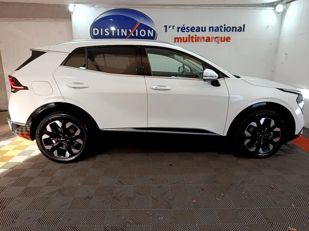 Profil côté gauche du KIA SPORTAGE blanc 2022 avec jantes noires et détails noirs sur les passages de roue.
