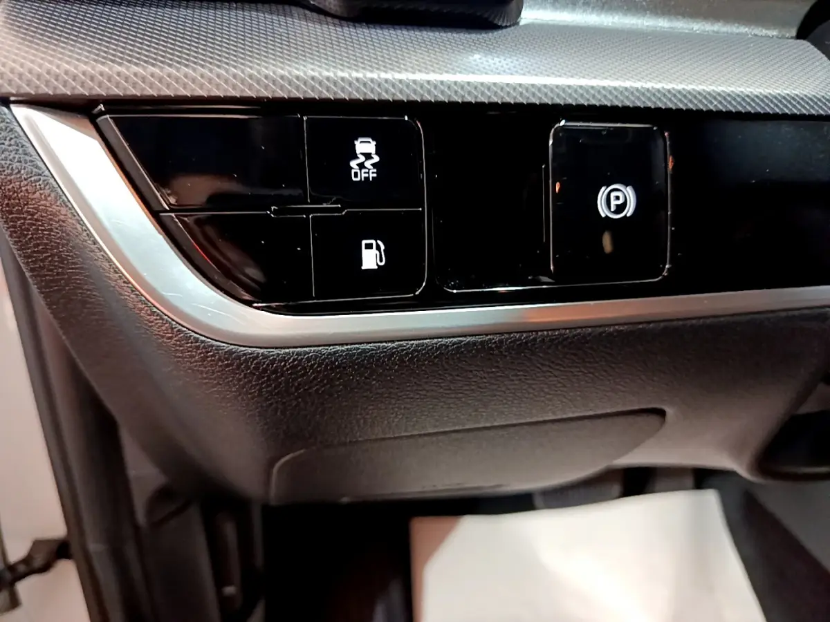 Gros plan sur les commandes noires du tableau de bord du Kia Sportage blanc 2022, avec bouton frein électrique et contrôle traction.