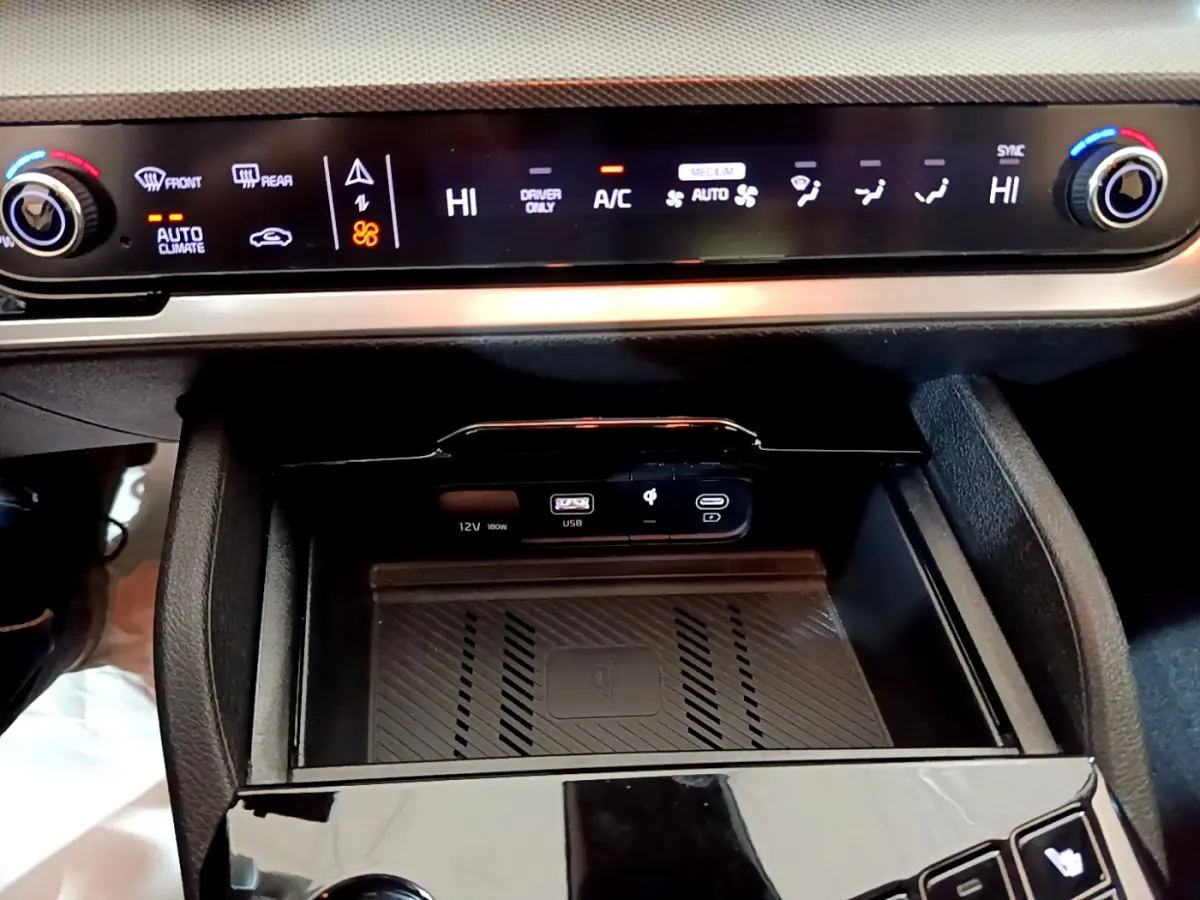 Détail de la console centrale du Kia Sportage blanc 2022 montrant la commande de climatisation digitale et la zone de recharge sans fil.